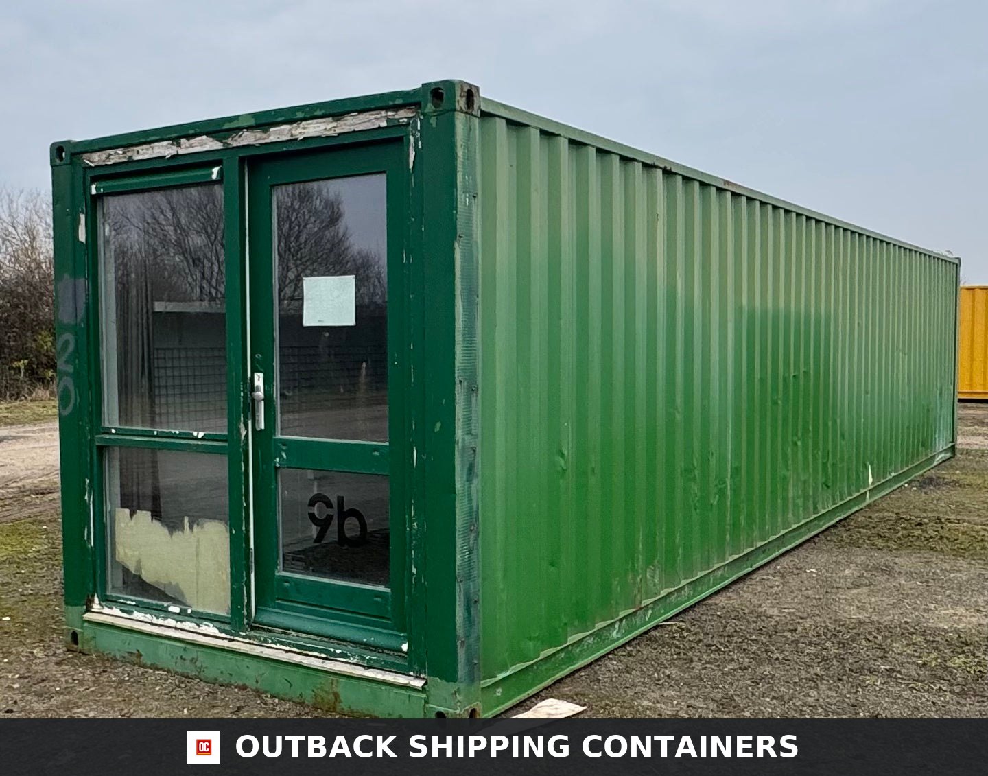 40 Ft Converted Shipping Container 40FT — Rear Exterior View | Outback Shipping Containers Exterior of a green 40ft converted shipping container with a glass entrance door and side window panel on a gravel lot