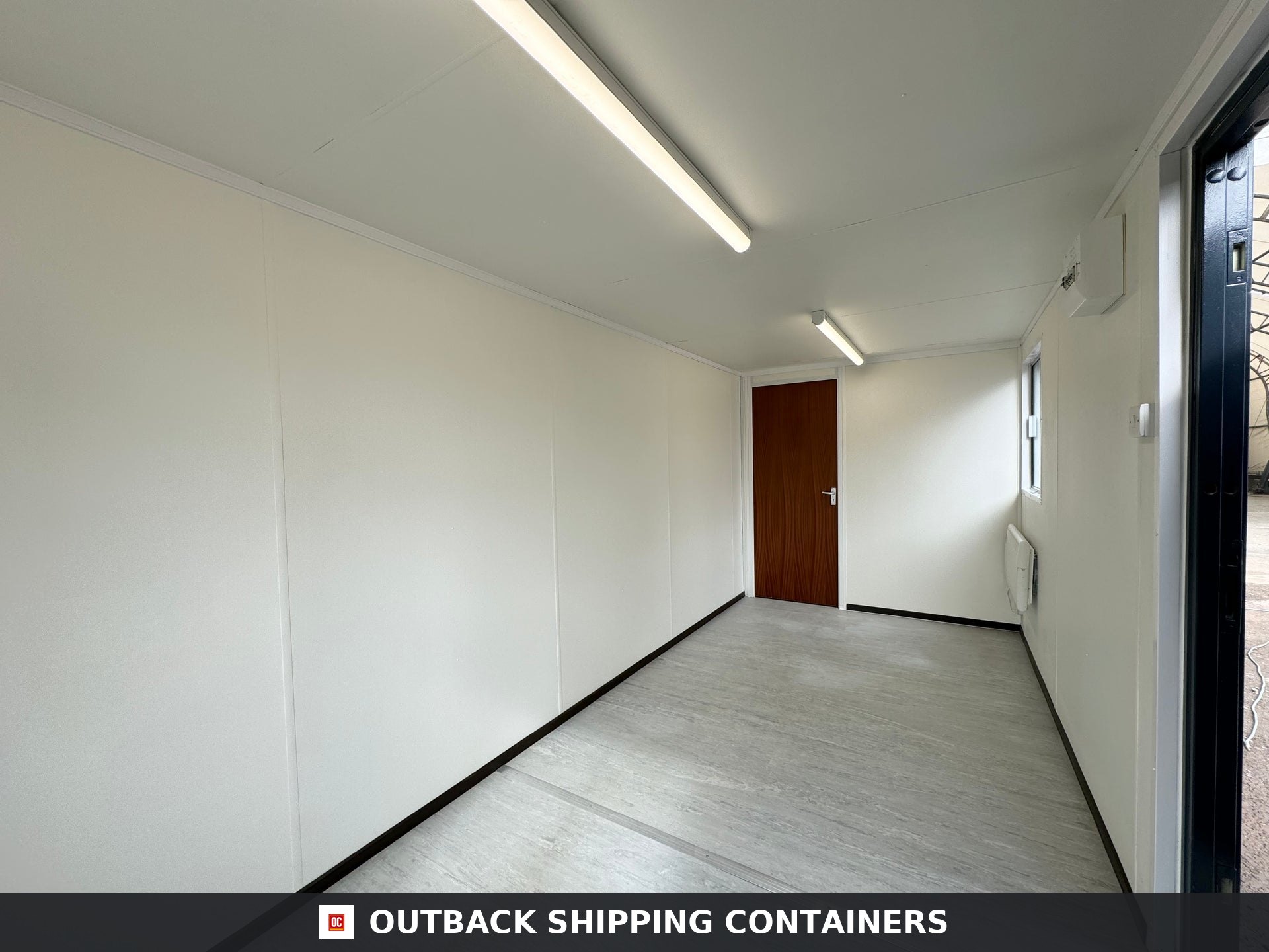 21x8ft for Sale — Window and Shutter Detail | Outback Shipping Containers 2 Interior of a refurbished 21ft shipping container office with white walls, grey flooring, and a wood grain door