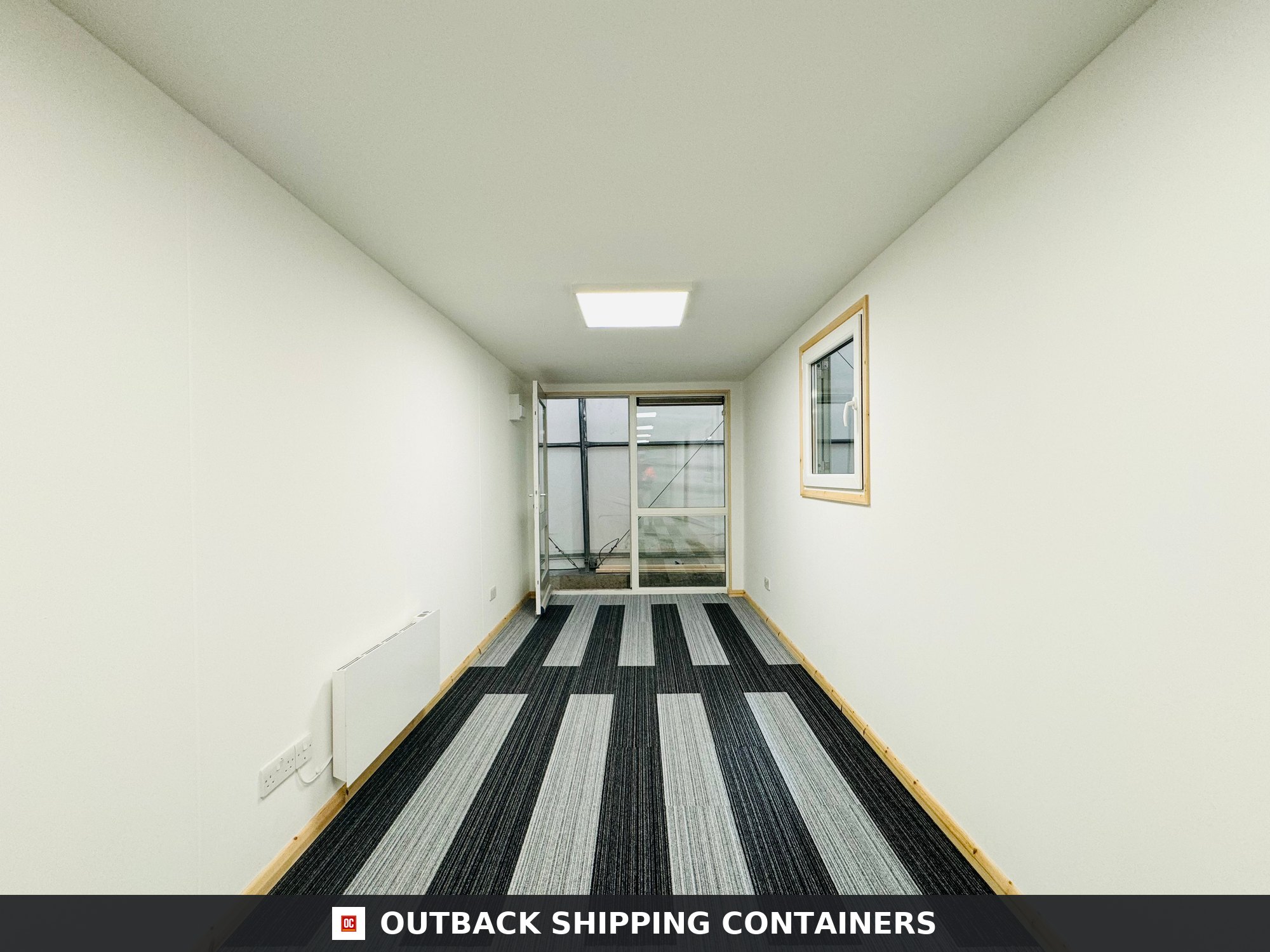 Interior view of a 40ft shipping container office with white walls, striped carpet tiles, and glass door entry