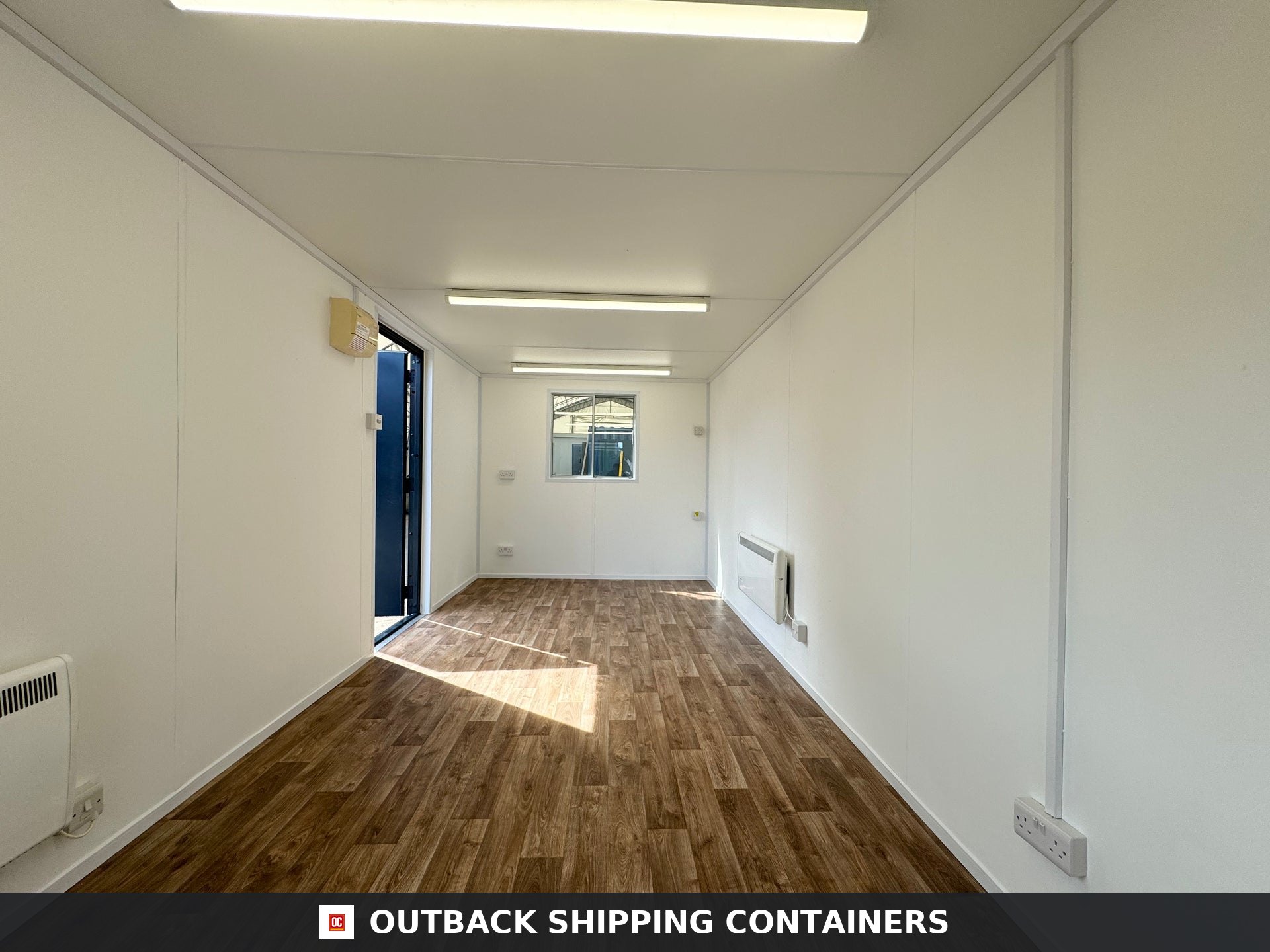 24x9 ft 24x9FT for Sale — Door and Entry Detail | Outback Shipping Containers Interior view of a 24x9 ft open plan portable office with white walls, vinyl wood flooring, and overhead lighting