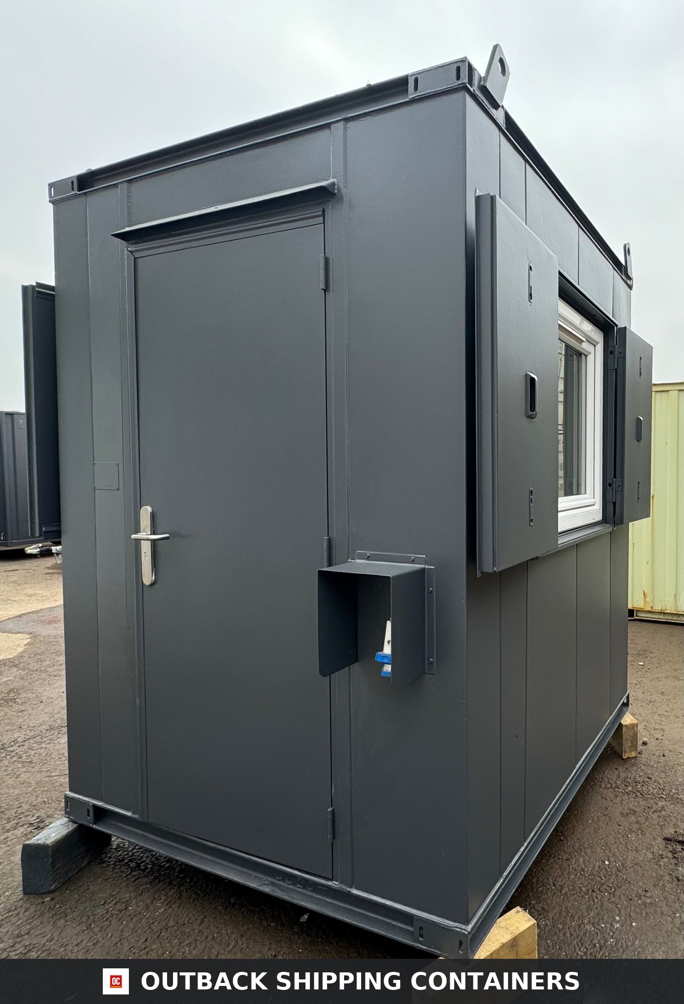 6x6 ft 6x6FT for Sale — Door and Entry Detail | Outback Shipping Containers Dark gray 6x6 gate house office with steel security door and open window shutters in a shipping container yard