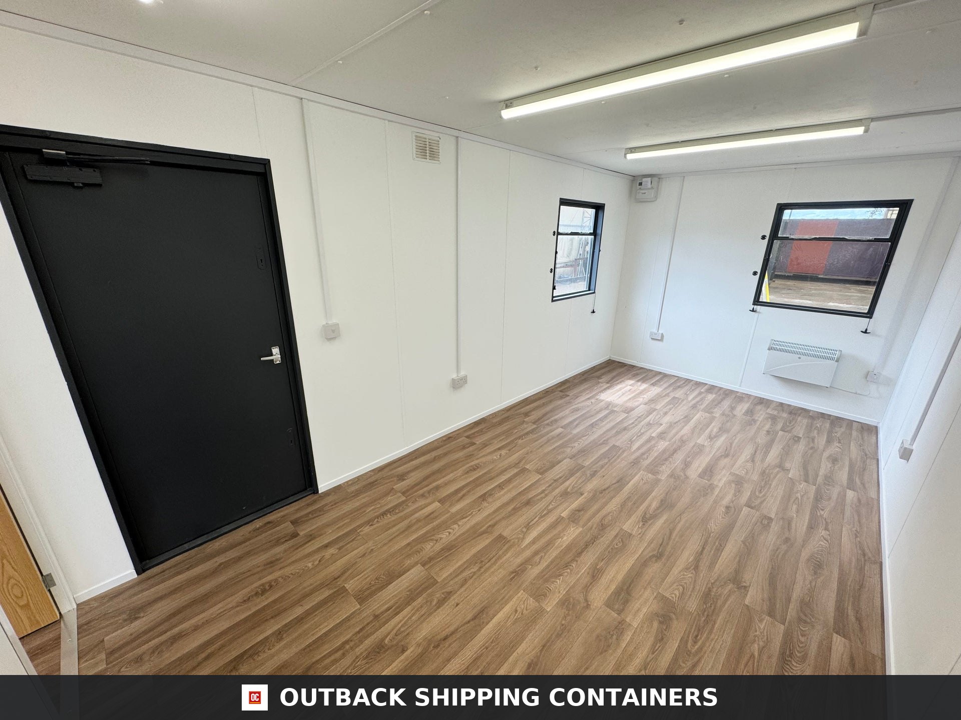 32x10 ft 32x10FT for Sale — Three-Quarter Angle View | Outback Shipping Containers Refurbished office interior of a 32x10 portable cabin with wood-style flooring, white walls, and a black steel door