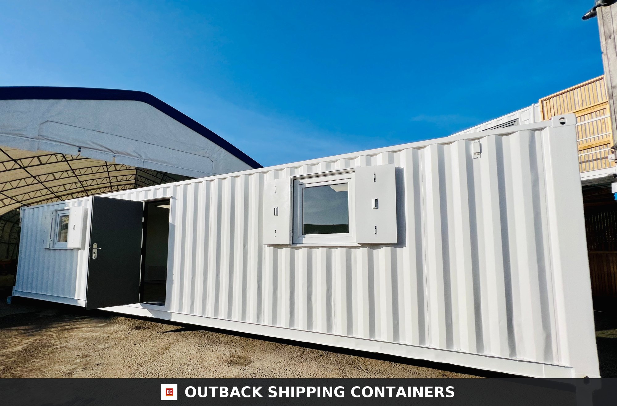 40ft white shipping container office conversion with open side door and shuttered windows under a bright blue sky