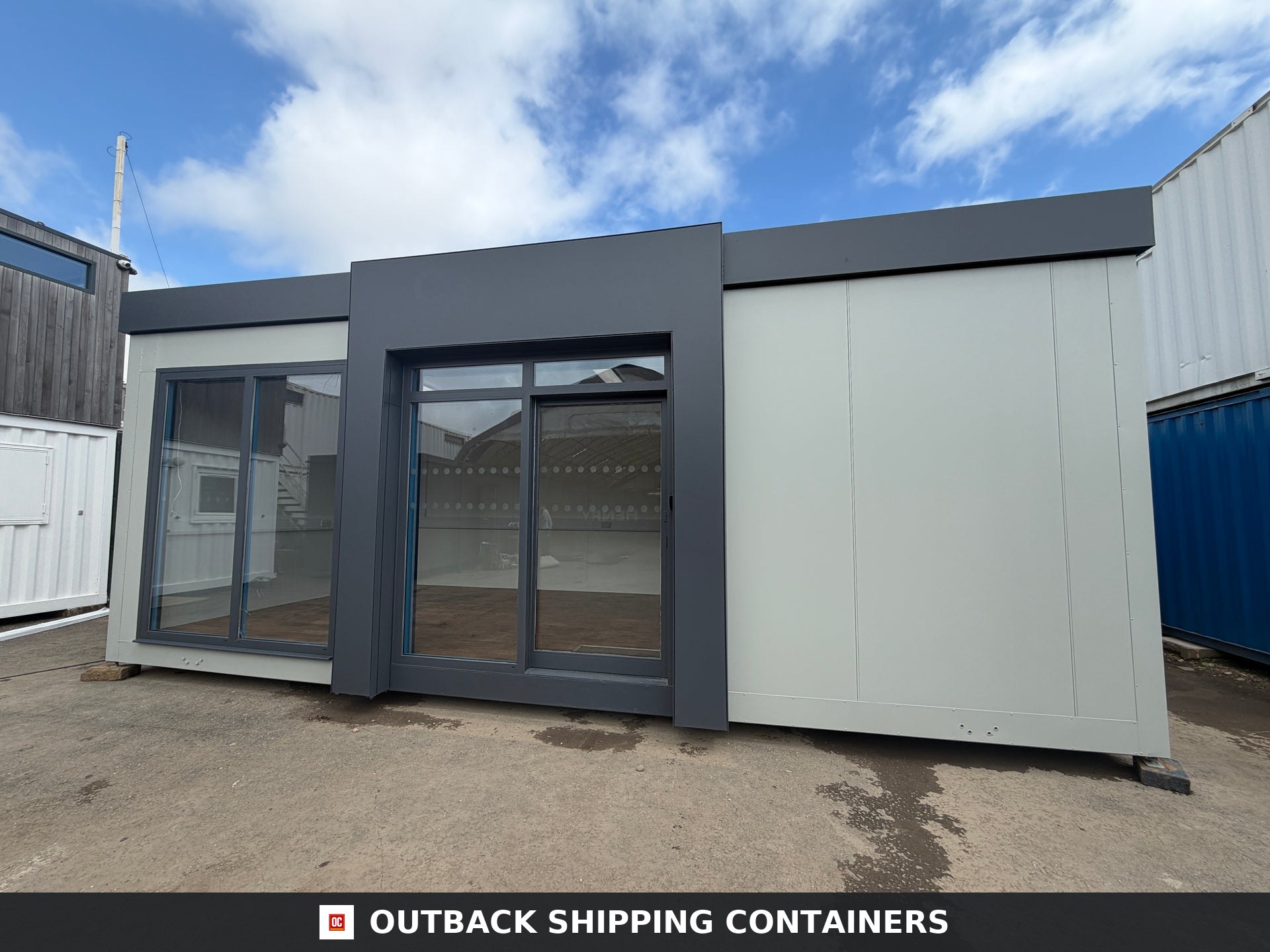 26x12ft for Sale — Interior View | Outback Shipping Containers 26ft refurbished marketing suite with light gray panels and dark anthracite window frames against a blue sky