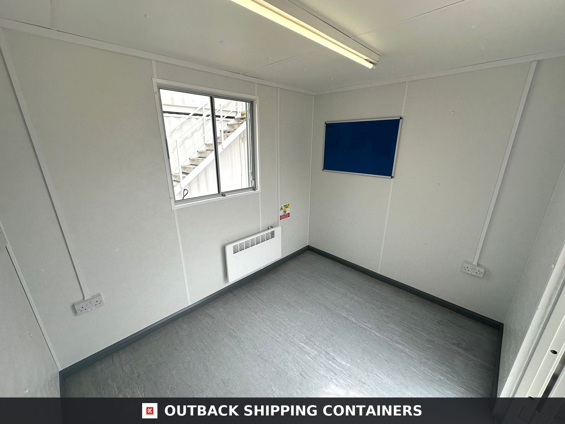 10x8 ft 10X8FT for Sale — Interior View | Outback Shipping Containers Interior view of a 10x8 portable office featuring white walls, a window, electric heater, and blue notice board