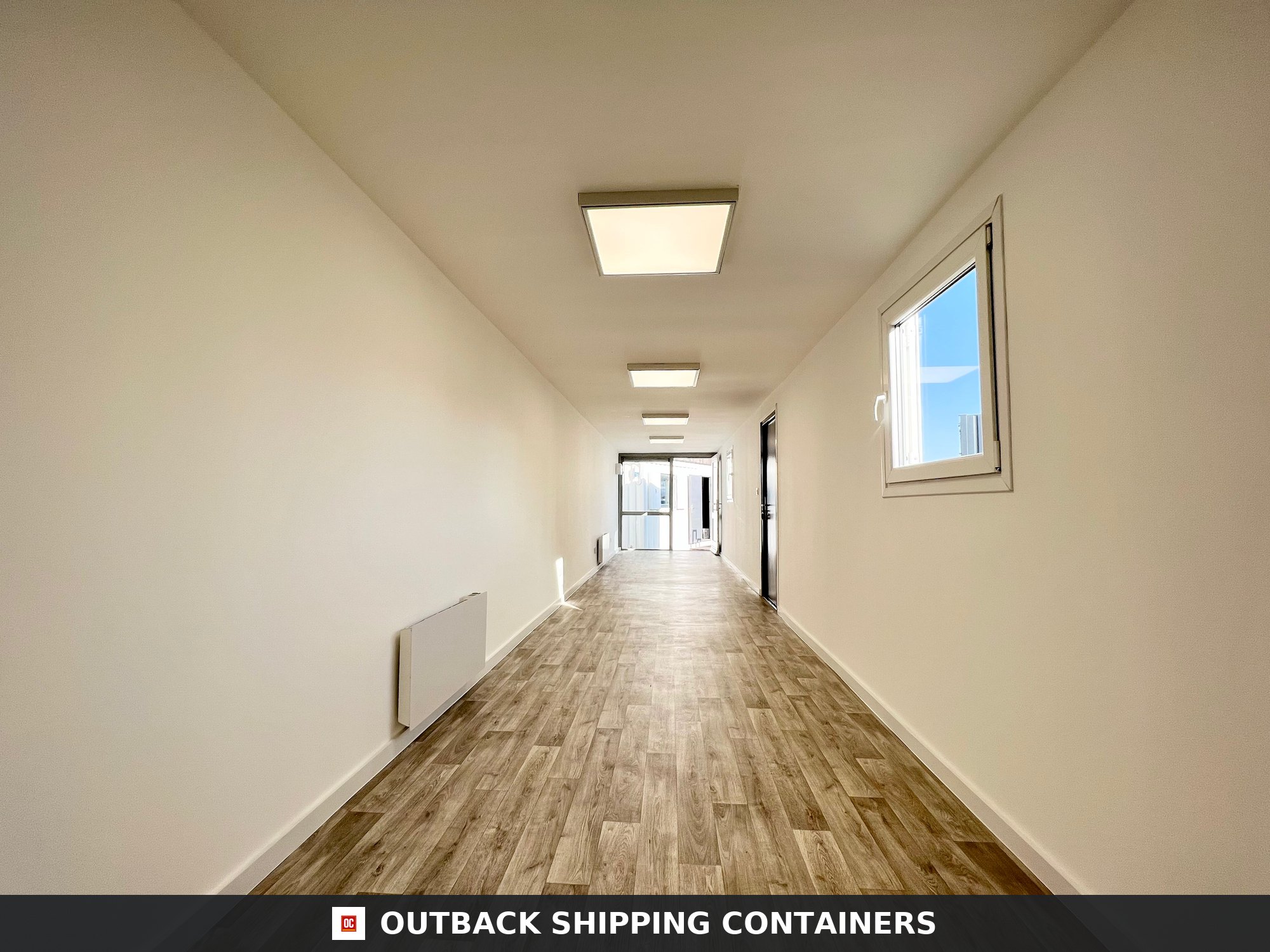 40ft shipping container office interior with wood-style flooring, white walls, overhead LED lights, and a window