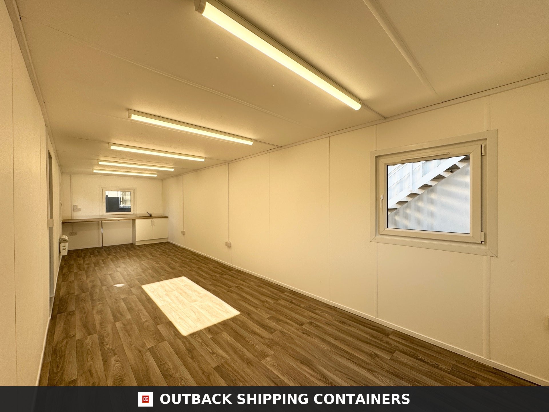 32x10ft Cabin for Sale — Interior Detail | Outback Shipping Containers Interior view of a 32x10ft open plan portable cabin showing wood-effect flooring and a white kitchenette area
