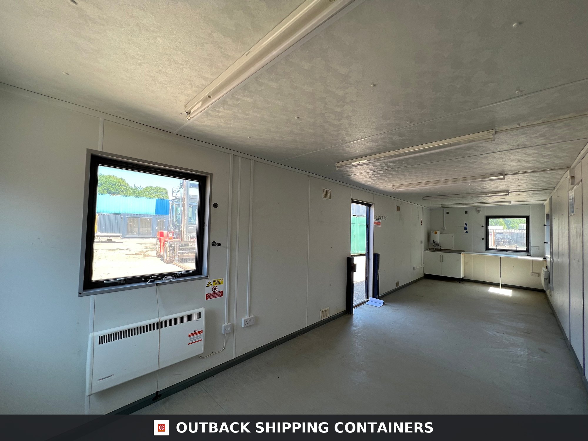 24x9 ft 24X9FT for Sale — Rear Exterior View | Outback Shipping Containers Open plan office interior of a 24x9 ft anti-vandal cabin with white walls, windows, and mounted heater