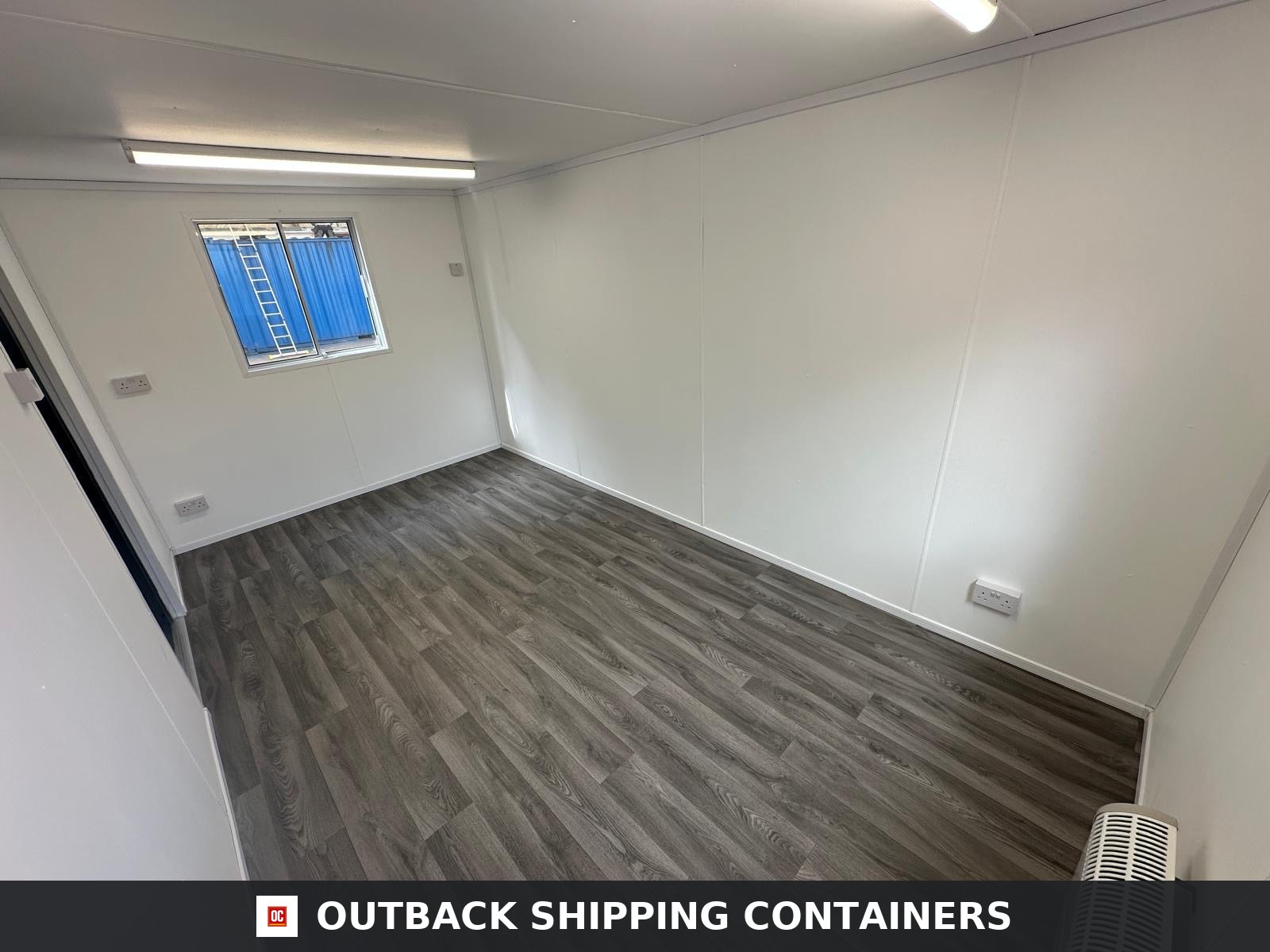16x9 ft 16x9FT for Sale — Interior Detail | Outback Shipping Containers Interior of a refurbished 16x9 portable office building featuring white walls, vinyl wood flooring, and overhead lighting