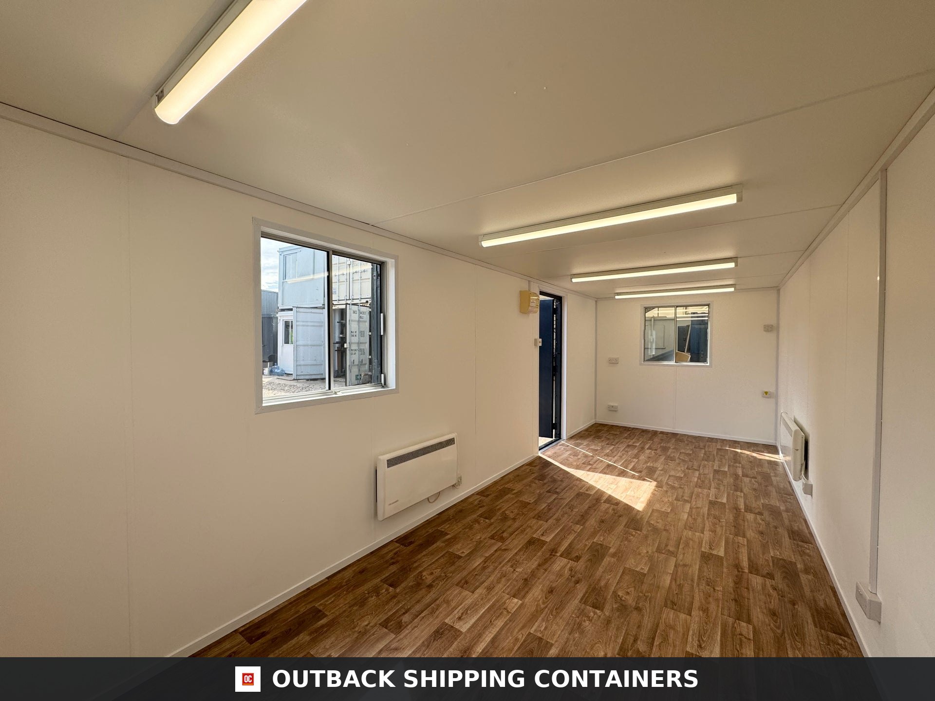 24x9 ft 24x9FT for Sale — Interior View | Outback Shipping Containers Interior of a refurbished 24x9 ft mobile office cabin with wood vinyl flooring white walls and fluorescent lights