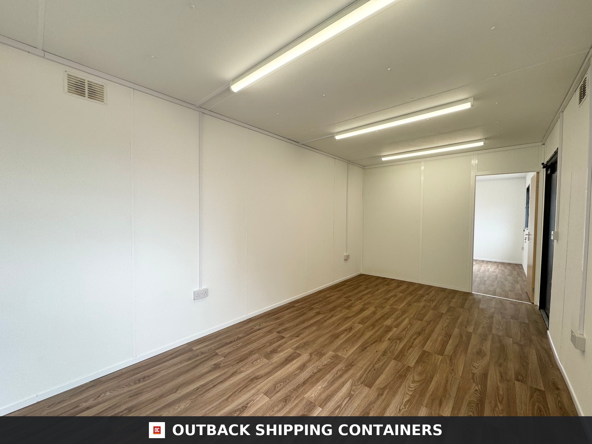 32x10 ft 32x10FT for Sale — Rear Exterior View | Outback Shipping Containers Interior of a refurbished 32x10 portable office with white walls, wood-effect flooring, and ceiling strip lighting