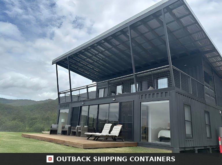 Three-quarter exterior view of the 3BHK two-storey container home with charcoal cladding, timber patio deck and cantilevered roof