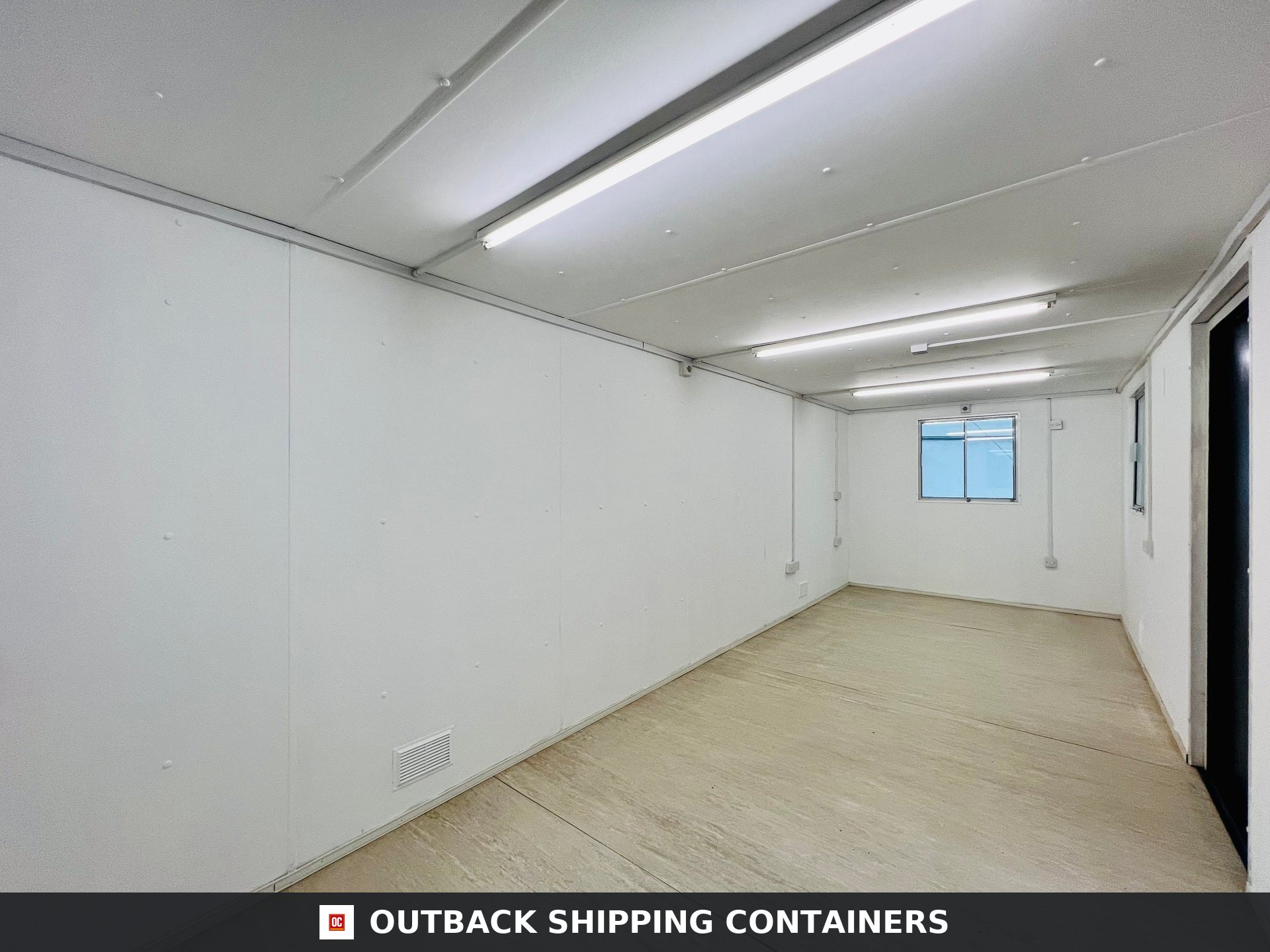 Interior view of a 24x9 ft shipping container office with white walls, linoleum flooring, and fluorescent ceiling lights