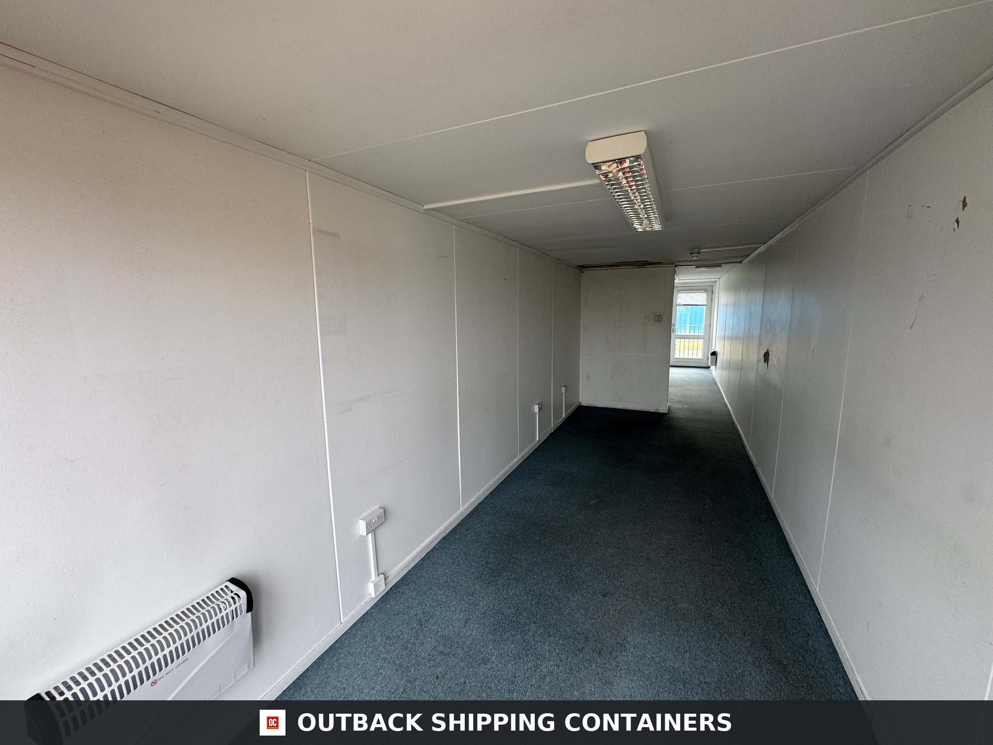 Converted Shipping Container 40 Ft 40FT — Side Profile View | Outback Shipping Containers Interior view of a 40 foot shipping container office with white paneled walls blue carpet and ceiling light