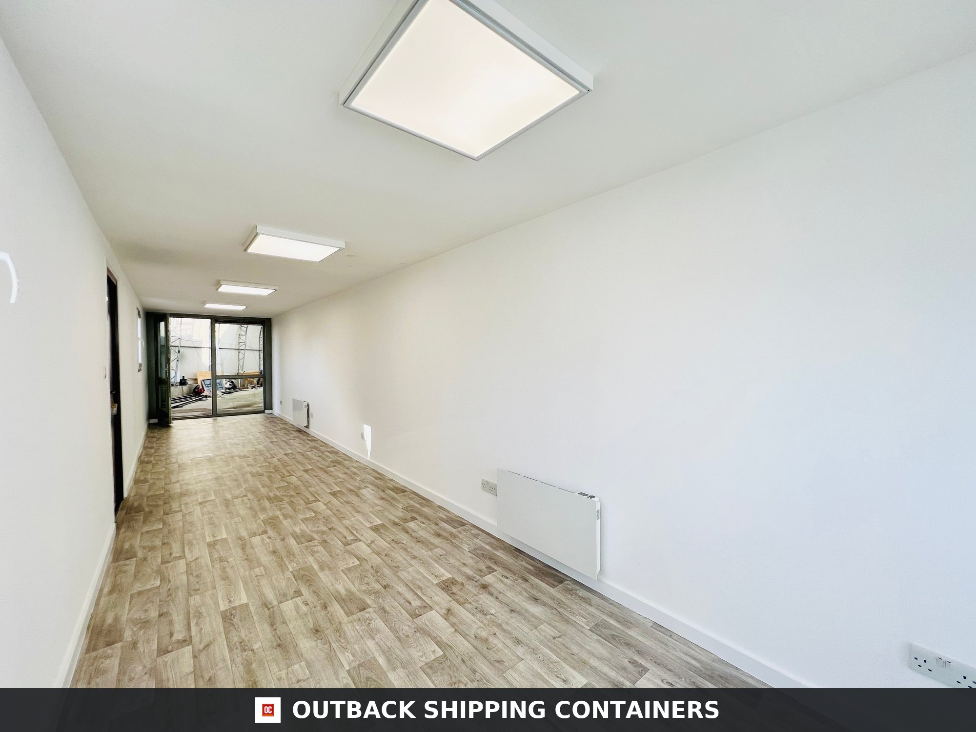 Interior view of a 40ft shipping container office with wood-style flooring white walls and square LED ceiling lights