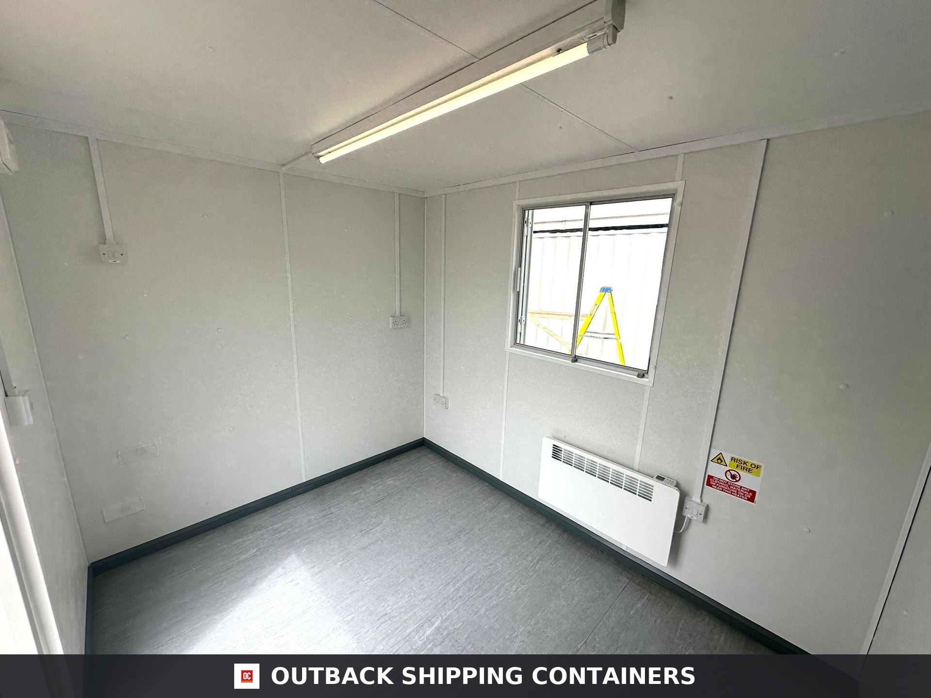 10x8 ft 10X8FT for Sale — Interior Detail | Outback Shipping Containers Interior view of 10x8 portable office unit with white walls, gray flooring, a window, heater, and overhead tube light