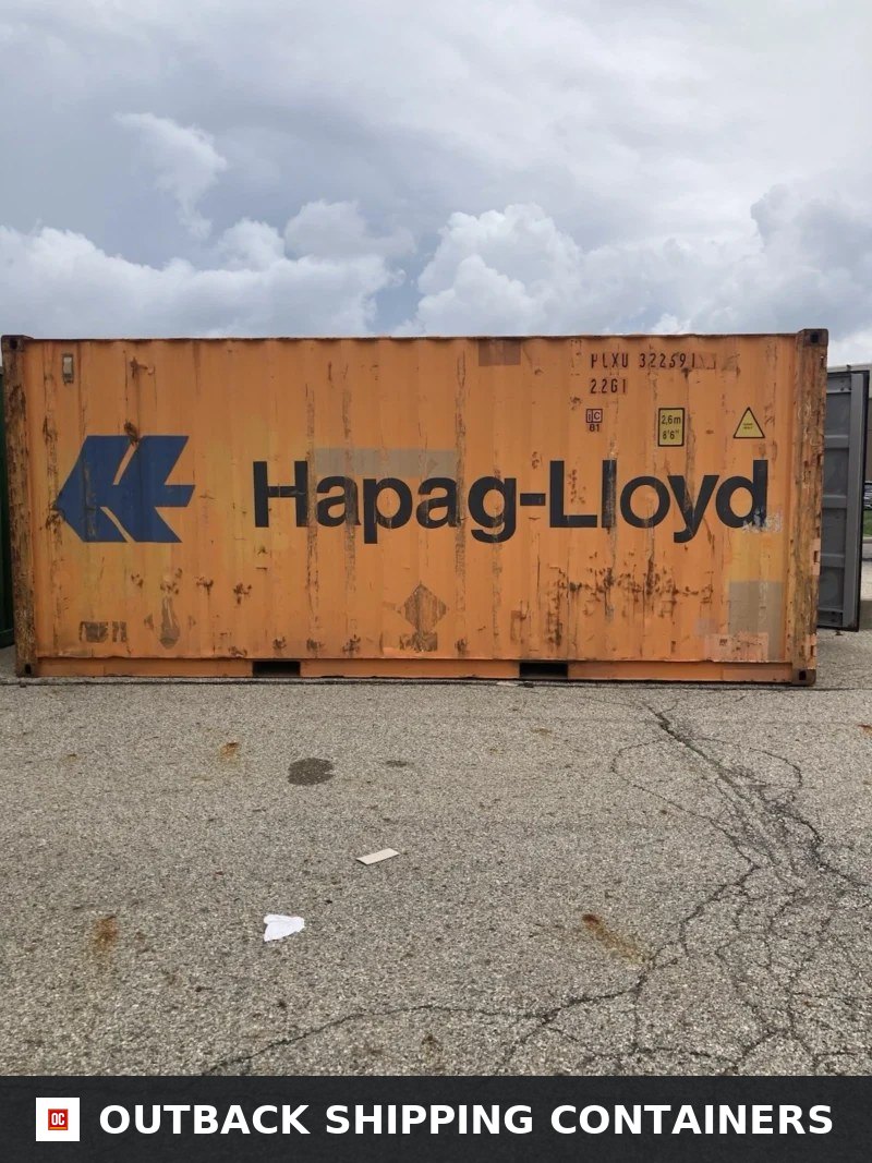 Orange 20ft Hapag-Lloyd shipping container with visible patina and blue logo resting on a paved lot