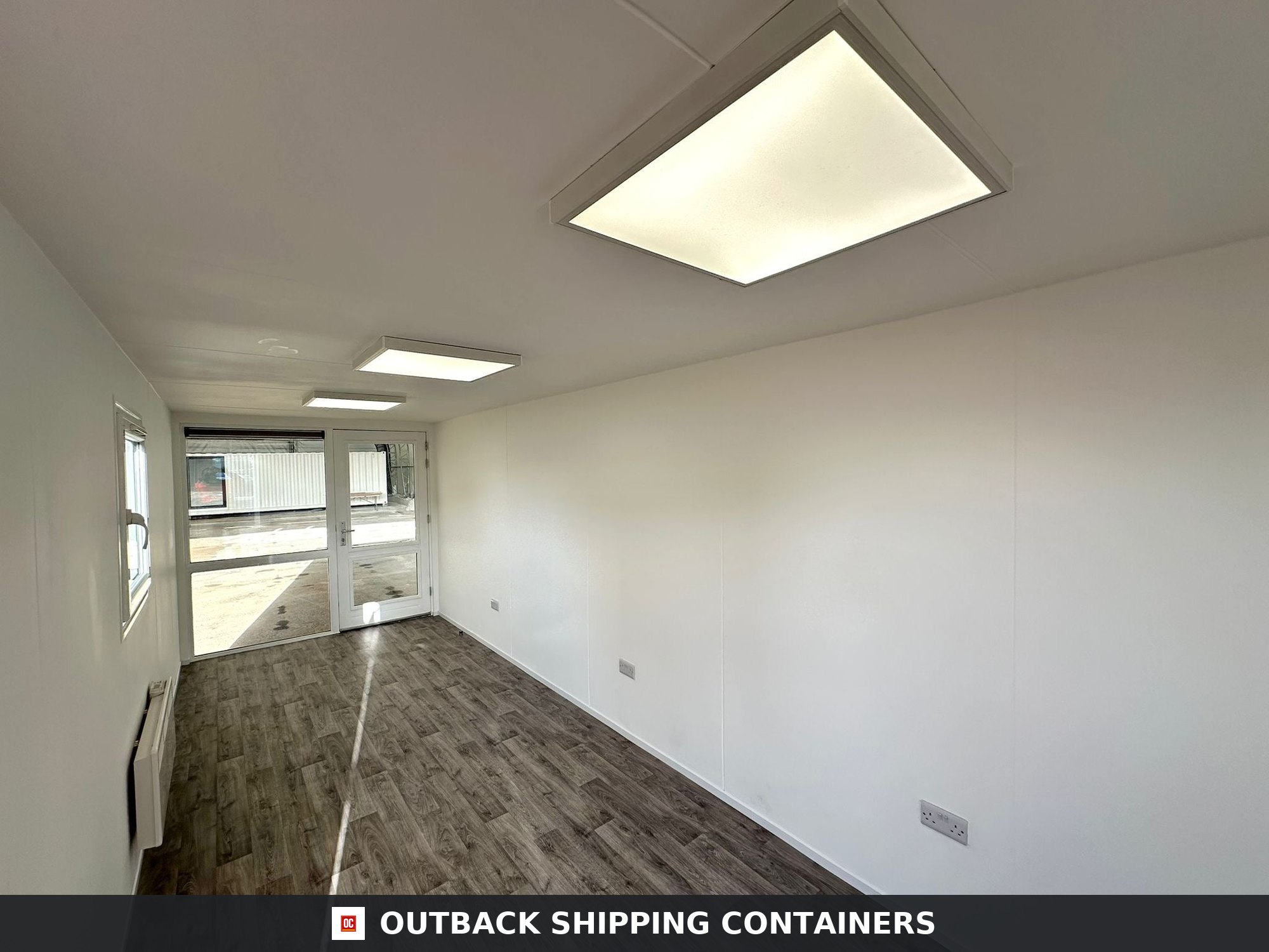 40ft shipping container office interior with white walls, wood-effect flooring, square LED ceiling lights, and glass door