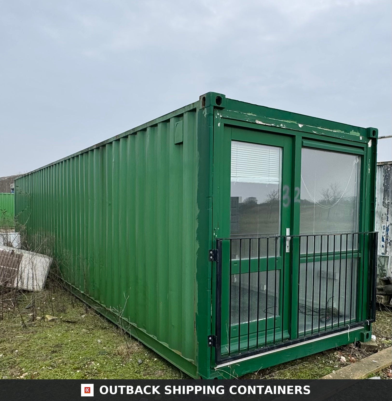 Converted Shipping Container 40 Ft 40FT — Rear Exterior View | Outback Shipping Containers 40ft green shipping container office with glass door and window protected by black metal bars on a grassy lot