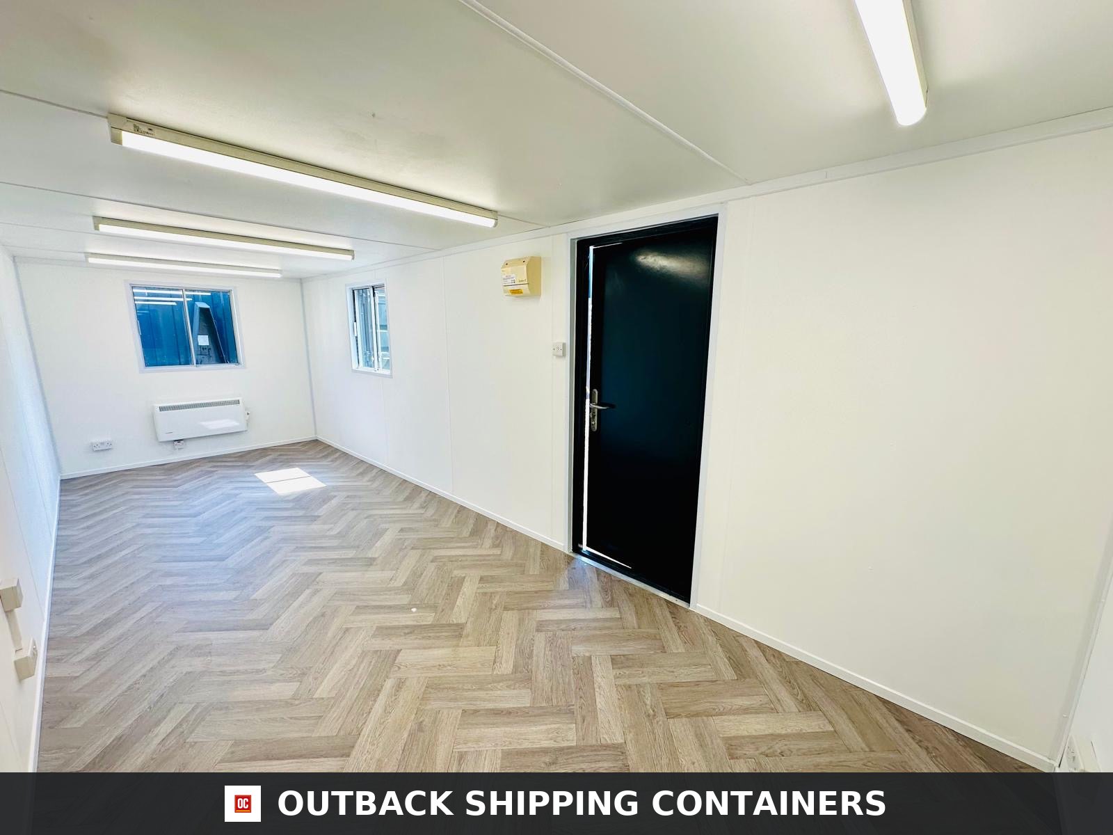 24x9 ft 24x9FT for Sale — Side Profile View | Outback Shipping Containers Interior of a refurbished 24x9 open plan office cabin with wood-pattern floors, white walls, and a black door