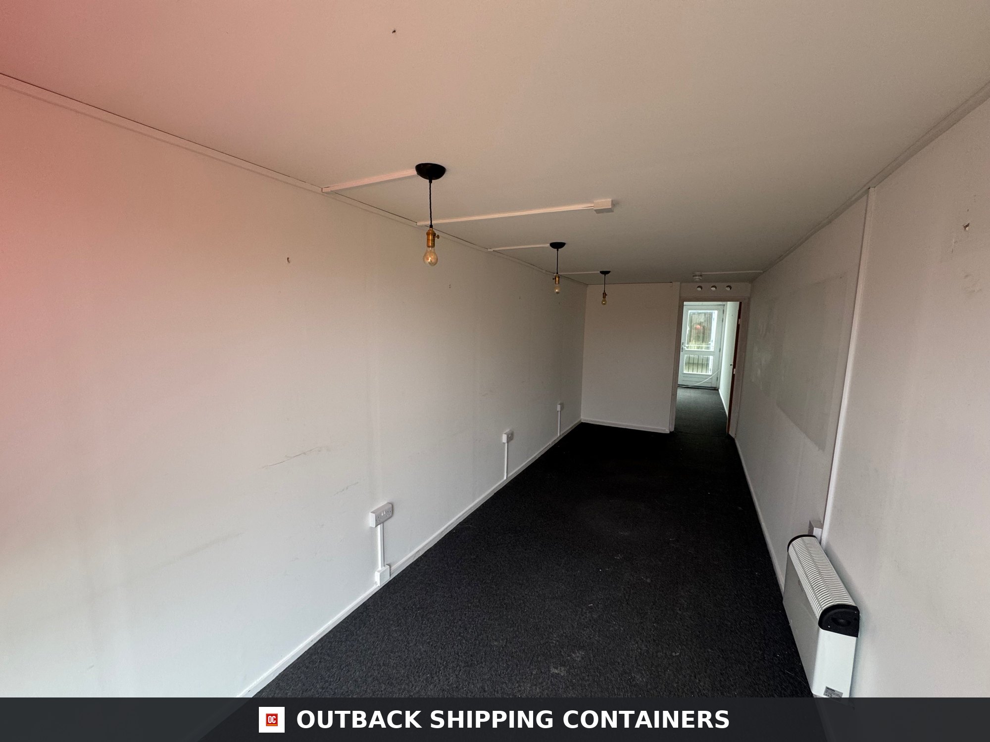 40 Ft Converted Shipping Container Home 40FT for Sale — Door and Entry Detail Interior view of a 40ft converted shipping container with white walls, black carpet, and hanging light bulbs