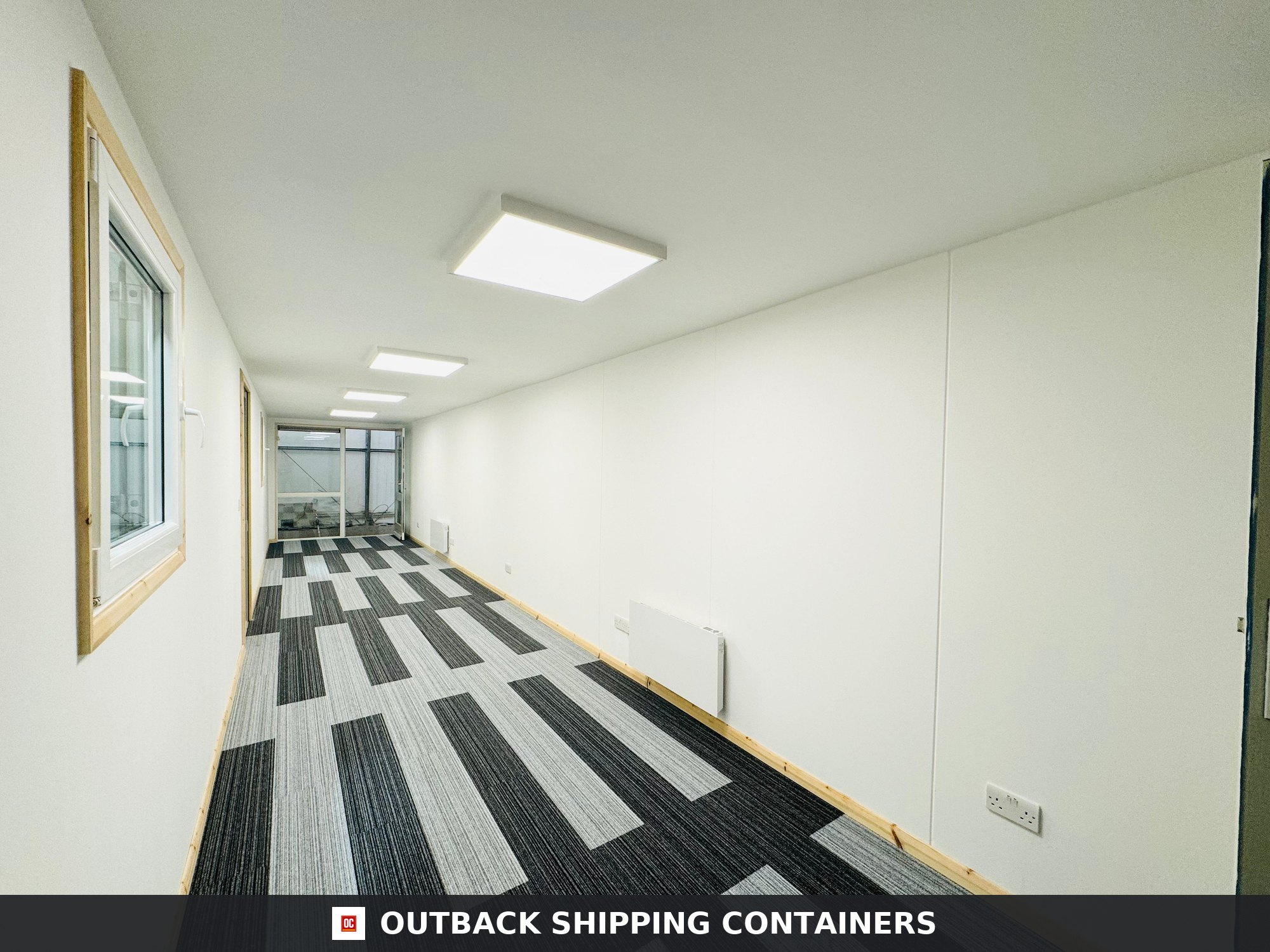 Interior view of a 40ft open plan shipping container office with striped carpet tiles and white panel walls