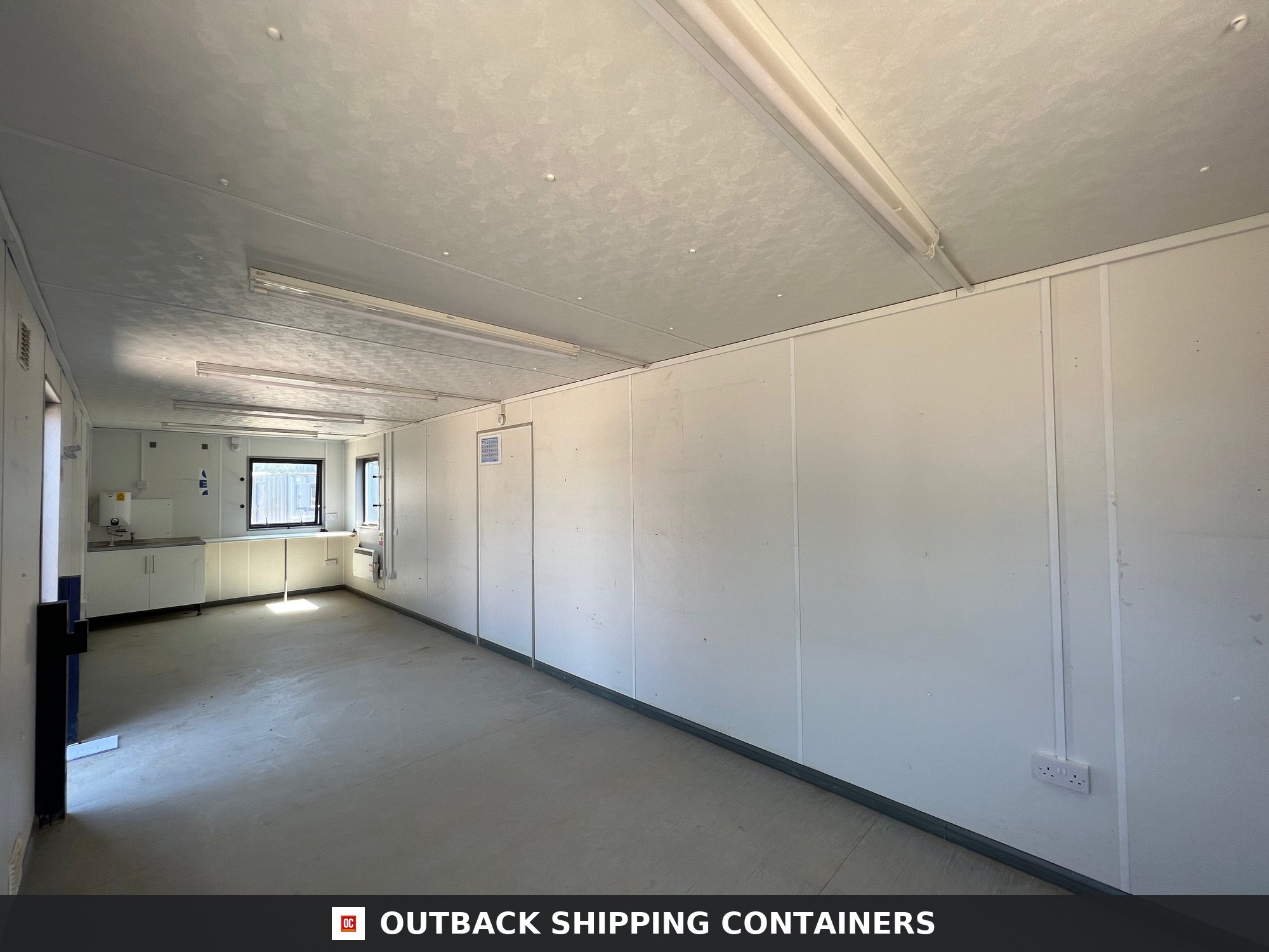 24x9 ft 24X9FT for Sale — Interior View | Outback Shipping Containers Interior view of a 24x9 open plan office cabin with white walls and a small kitchen area in the back corner