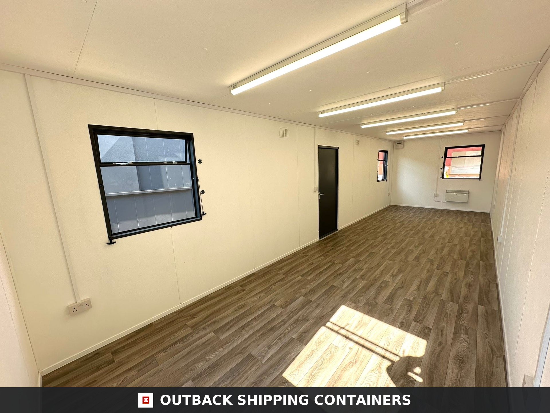 32x10ft Cabin for Sale — Interior View | Outback Shipping Containers 2 3 Interior view of an open plan 32ft office cabin with wood-effect flooring, beige walls, and fluorescent ceiling lights