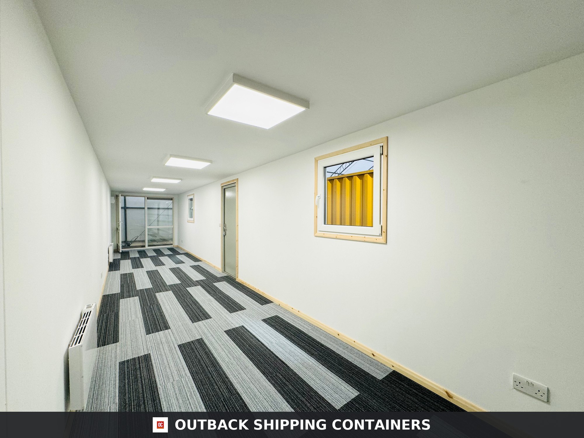 Interior of a 40ft shipping container office with white walls, carpet tiles, LED lights, and a small window