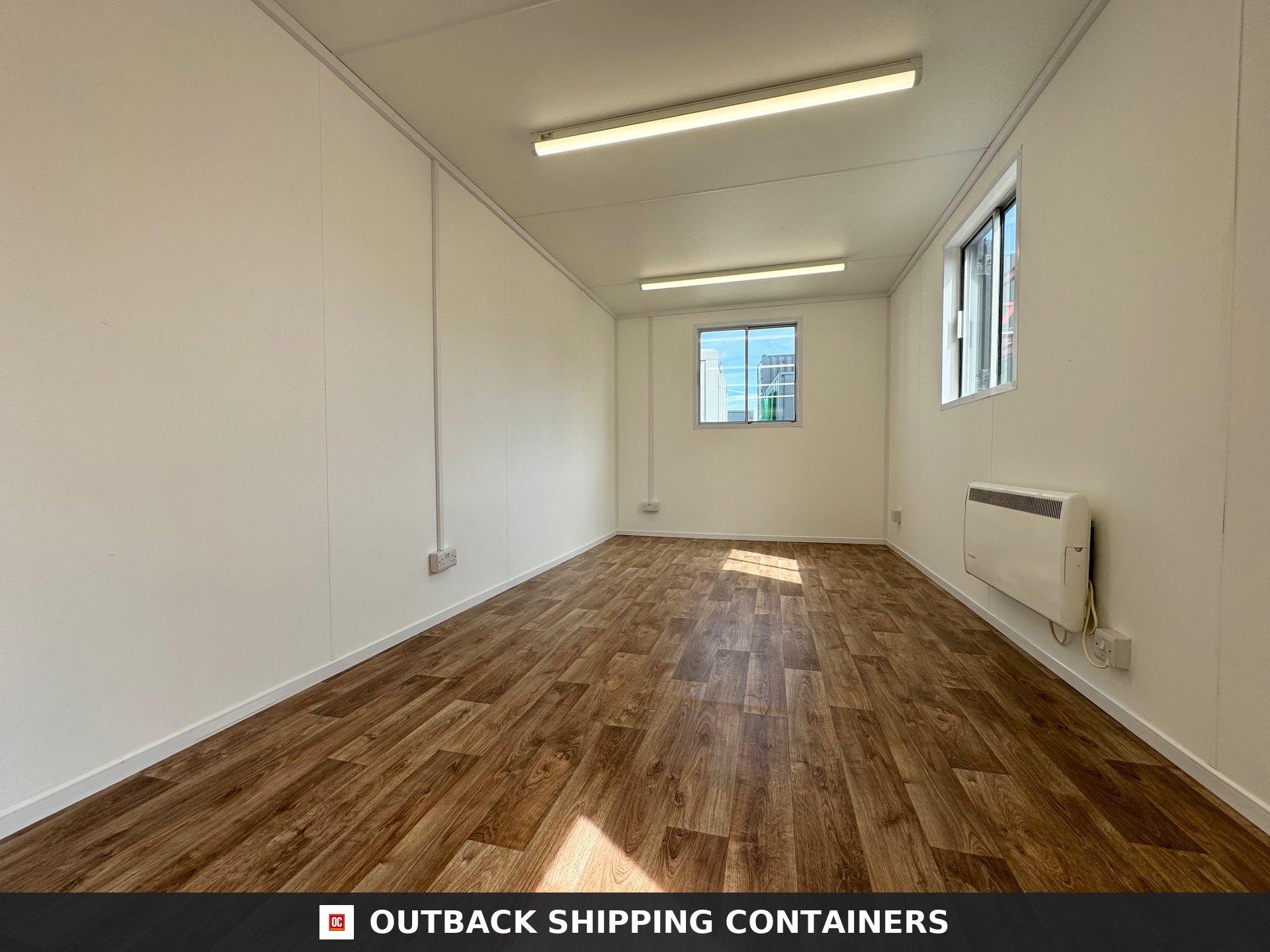 24x9 ft 24x9FT for Sale — Rear Exterior View | Outback Shipping Containers Interior view of an empty 24x9 ft mobile office cabin with wood laminate flooring and white paneled walls