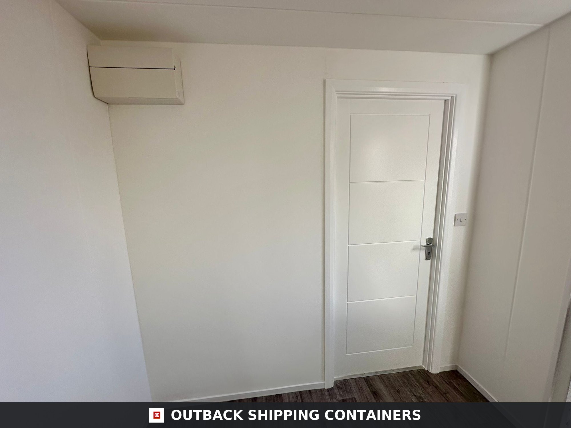Interior view of a converted shipping container office with white walls and a white paneled internal door