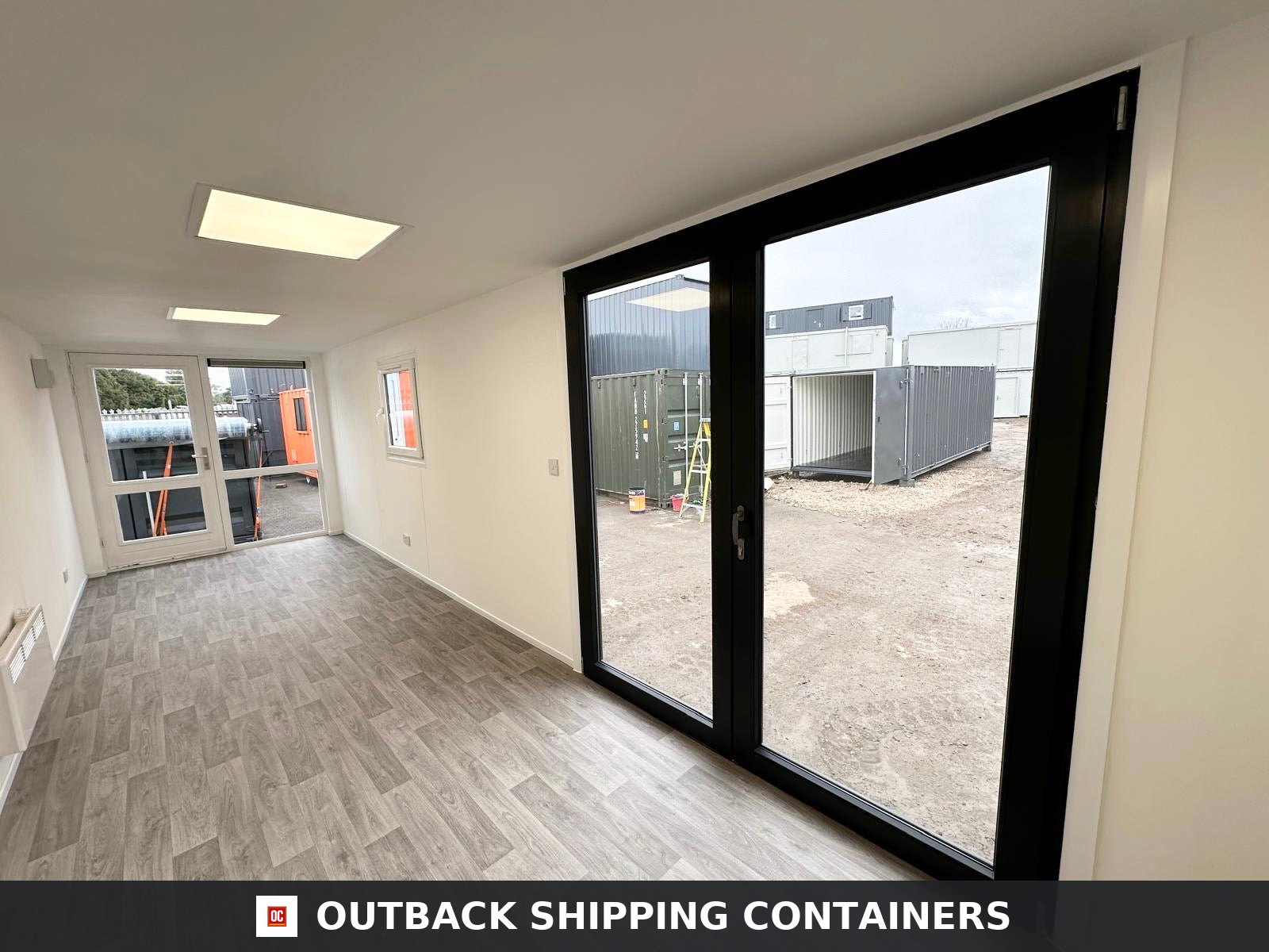 40ft shipping container office interior with wood-style flooring and large black double glass doors looking outside