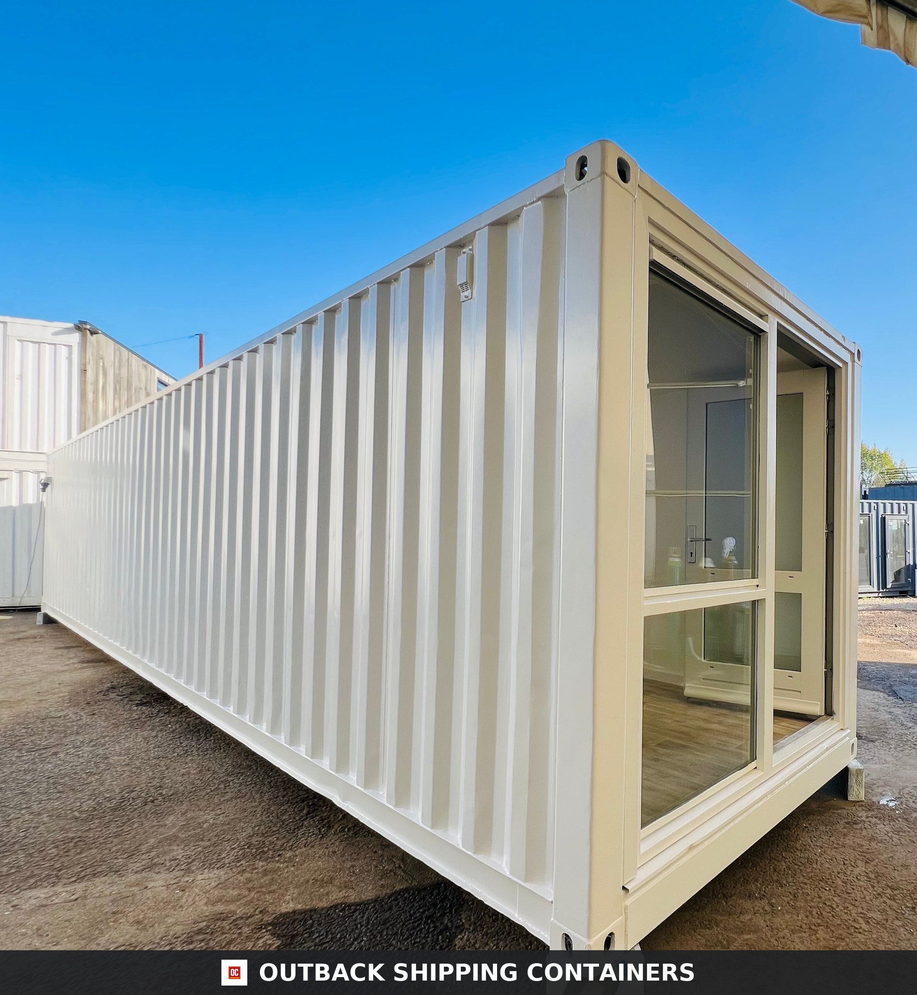 40ft white converted shipping container office with large glass windows and corrugated steel walls under a blue sky