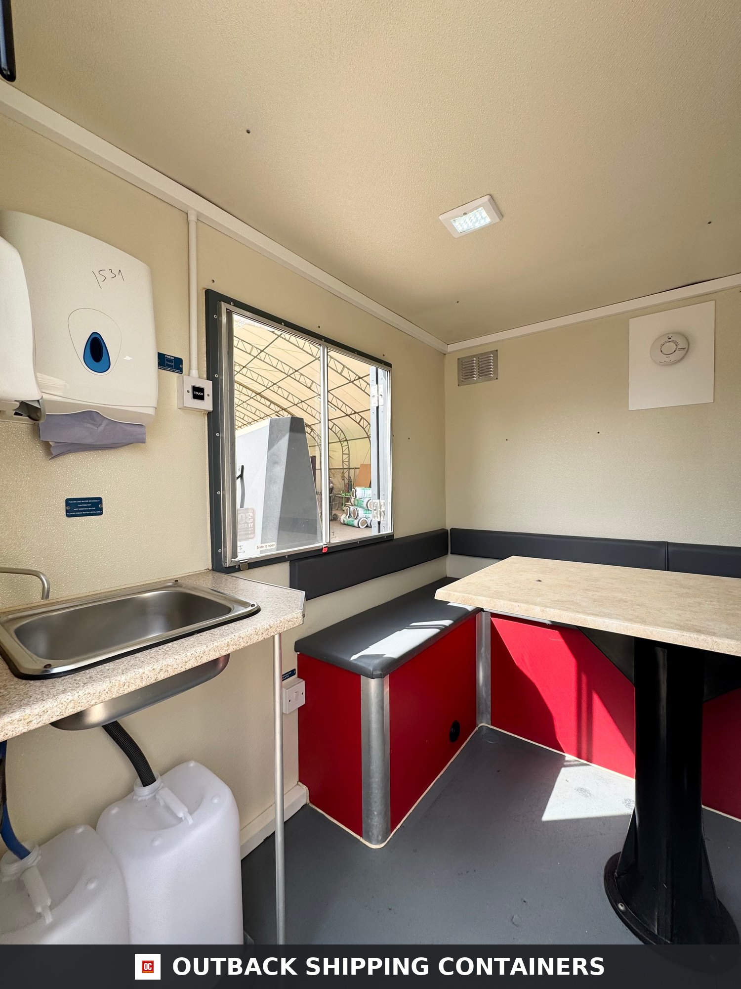 Groundhog Towable Mobile Welfare | 16 Ft | 2017 |Twin Axle | GPO500 — Three-Quarter Angle View Groundhog towable mobile welfare unit interior with stainless steel sink dining table and red bench seating