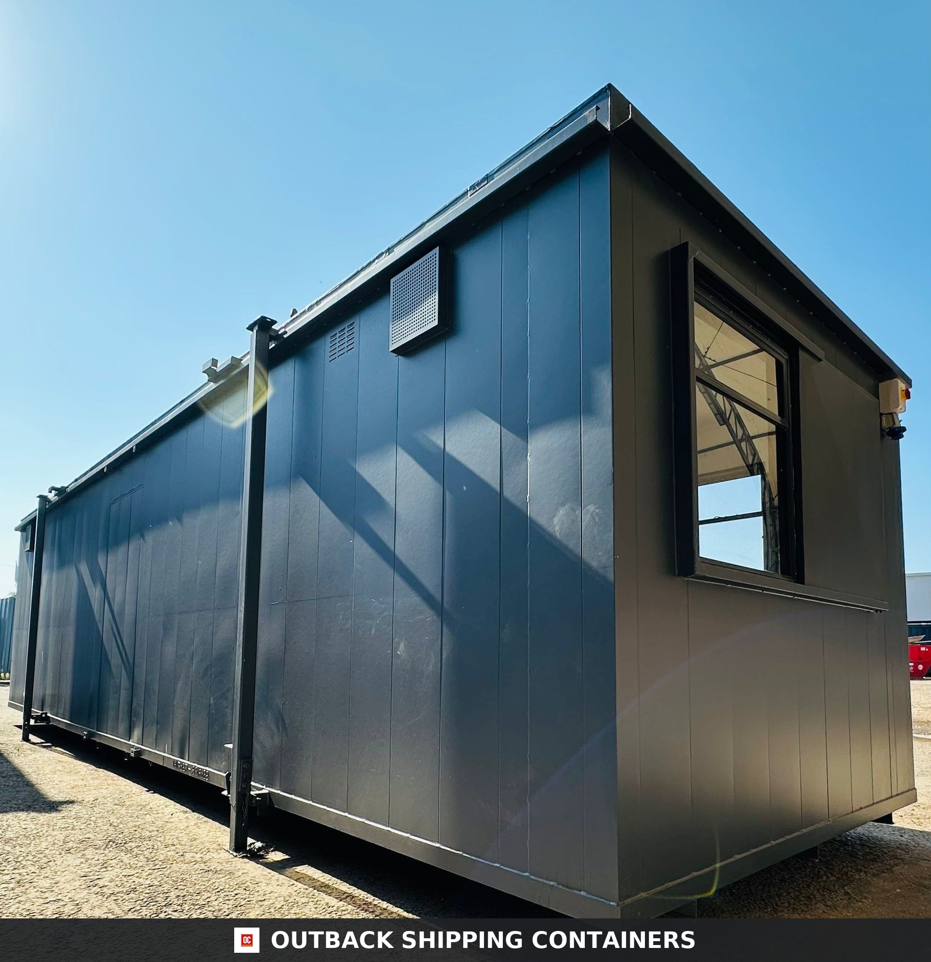 32x10ft Cabin for Sale — Window and Shutter Detail | Outback Shipping Containers 2 3 Exterior view of a dark grey 32x10ft anti-vandal portable cabin with window and ventilation port under a blue sky