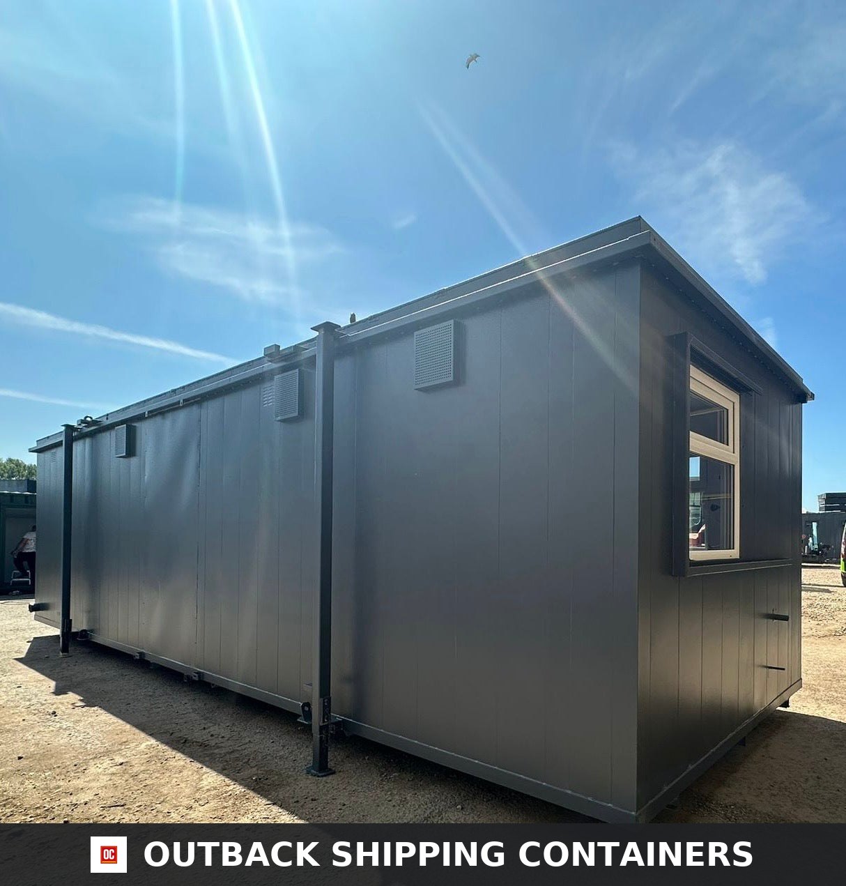 Rear and side view of a grey refurbished 32ft shipping container cabin with a white frame window under a sunny sky