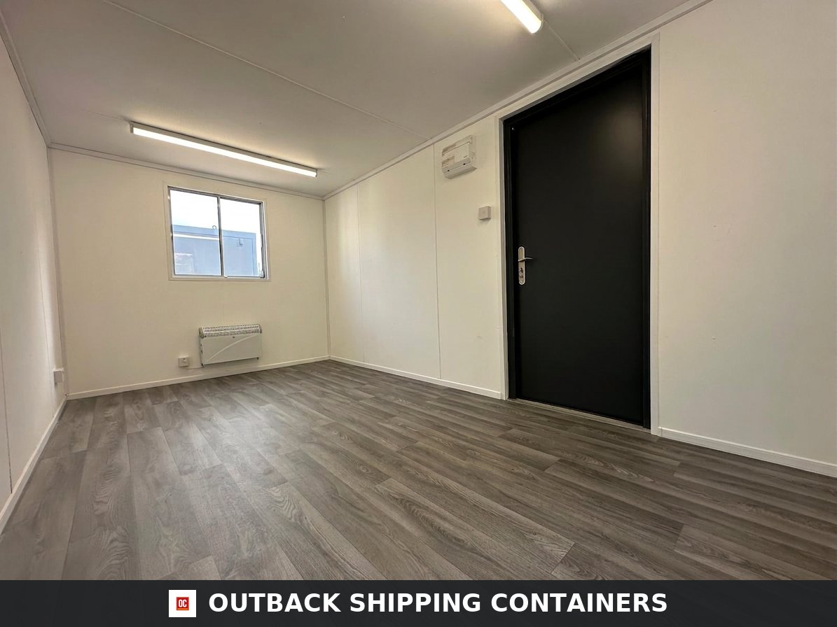 16x9 ft 16x9FT for Sale — Side Profile View | Outback Shipping Containers Interior of a refurbished 16x9 portable office with white walls, wood-look flooring, electric heater, and black door