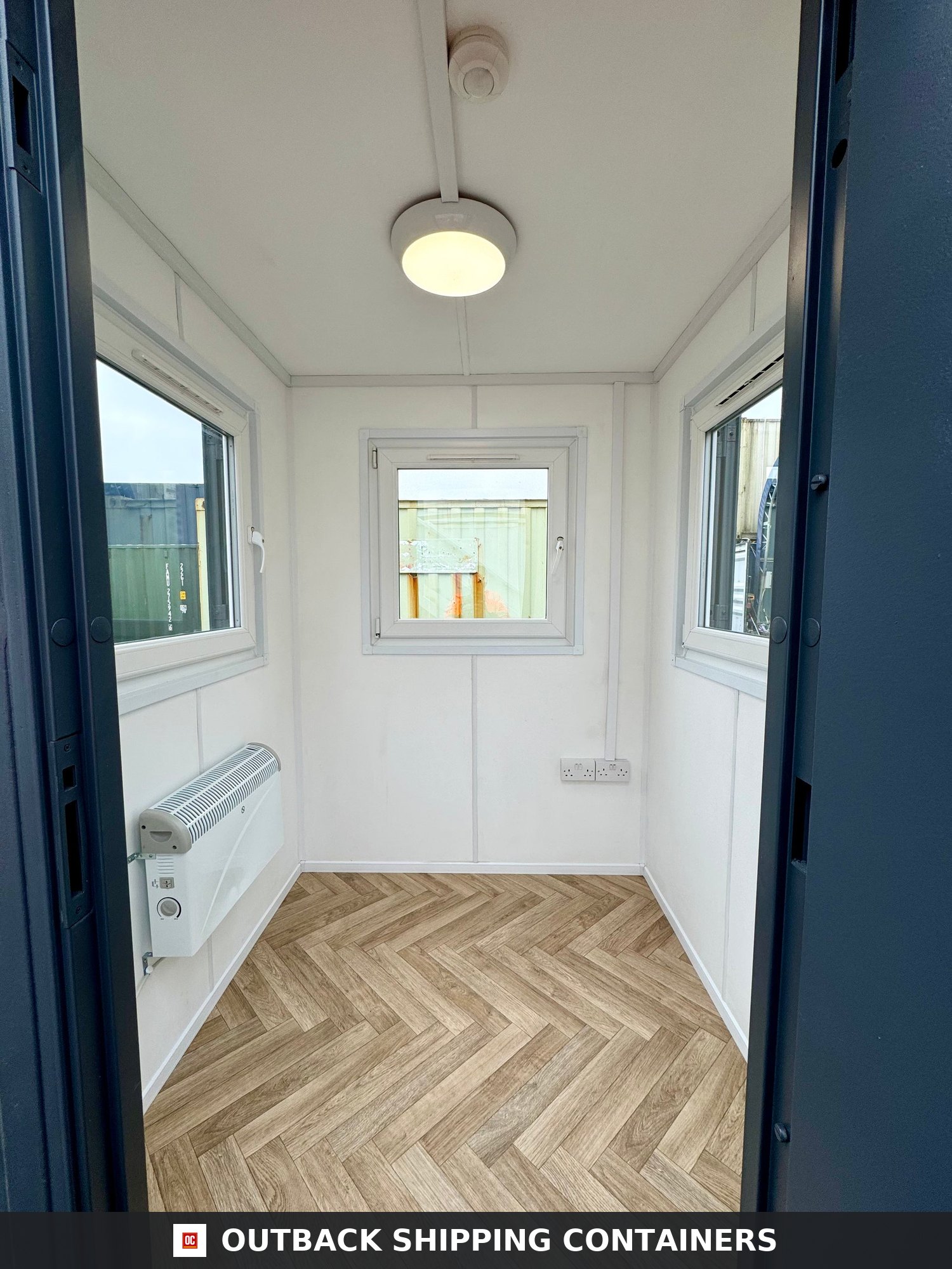 6x6 ft 6x6FT for Sale — Interior View | Outback Shipping Containers Inside a 6x6 gate house office featuring white walls wood-style herringbone flooring and three windows