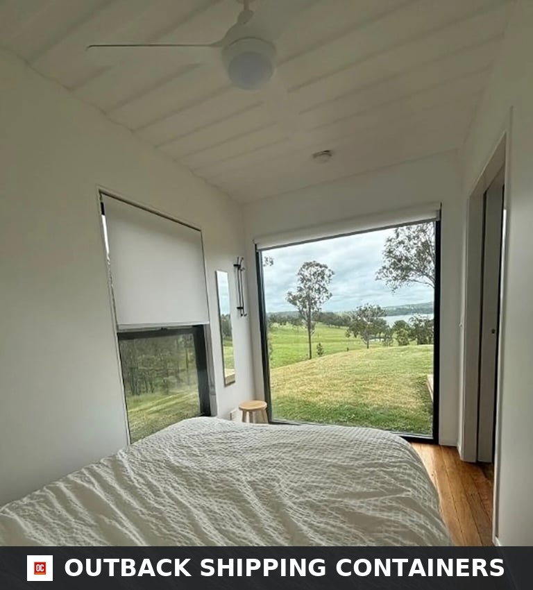 Guest bedroom inside the 3BHK container home with queen bed and floor-to-ceiling picture window overlooking open countryside