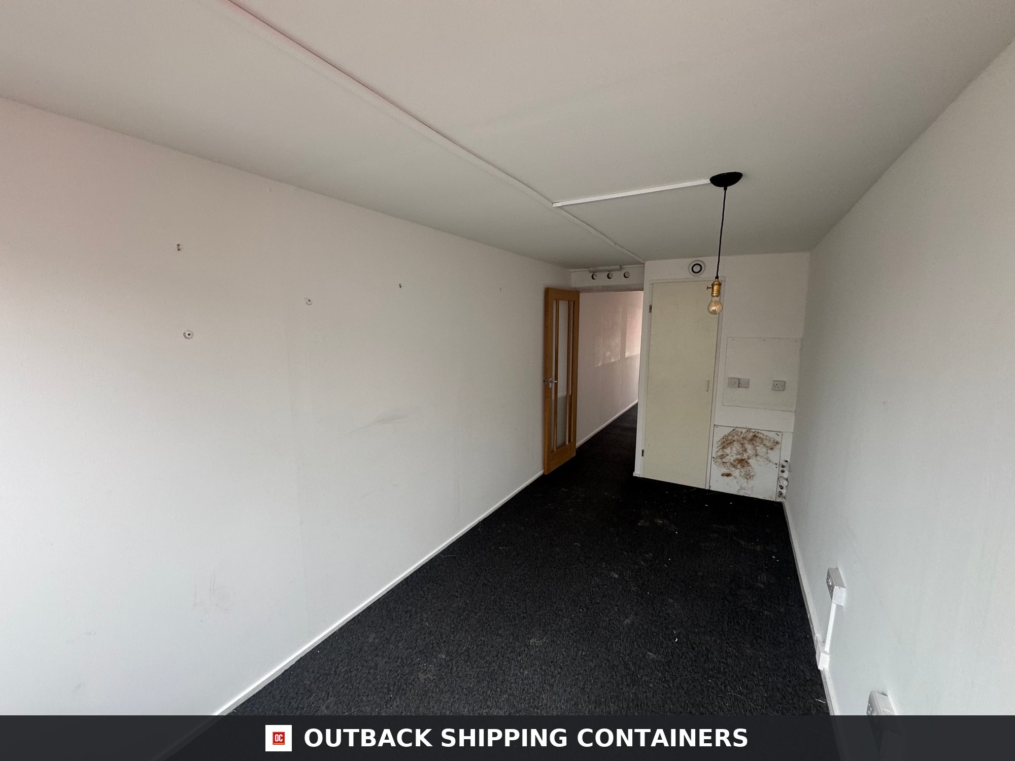 40 Ft Converted Shipping Container Home 40FT — Rear Exterior View | Outback Shipping Containers 40ft shipping container home interior with white walls, black carpet, and a wooden glass-paneled door