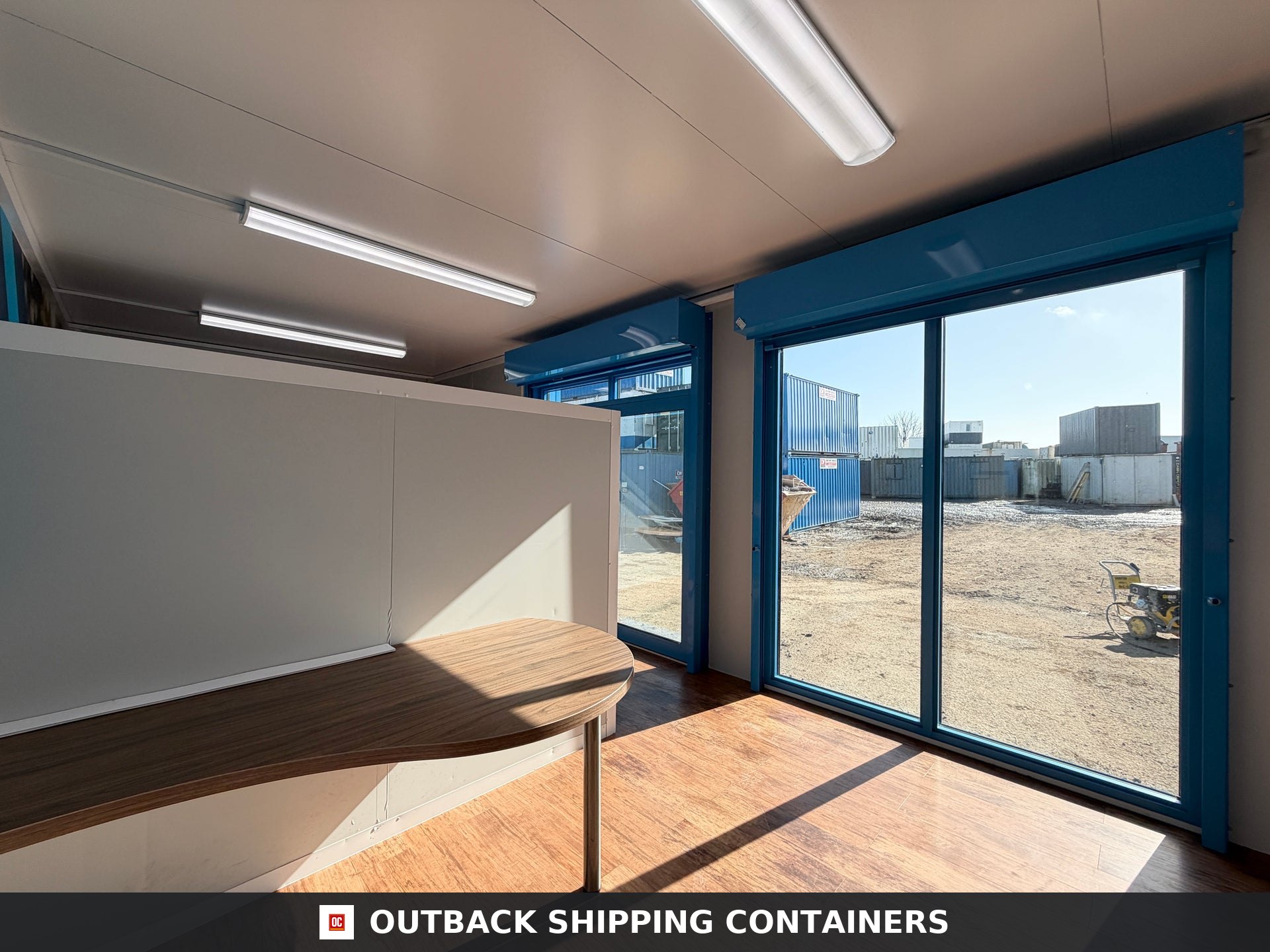 26x12ft for Sale — Three-Quarter Angle View | Outback Shipping Containers Interior of a refurbished 26x12ft portable marketing suite with wood flooring, blue window frames, and glass sliding doors