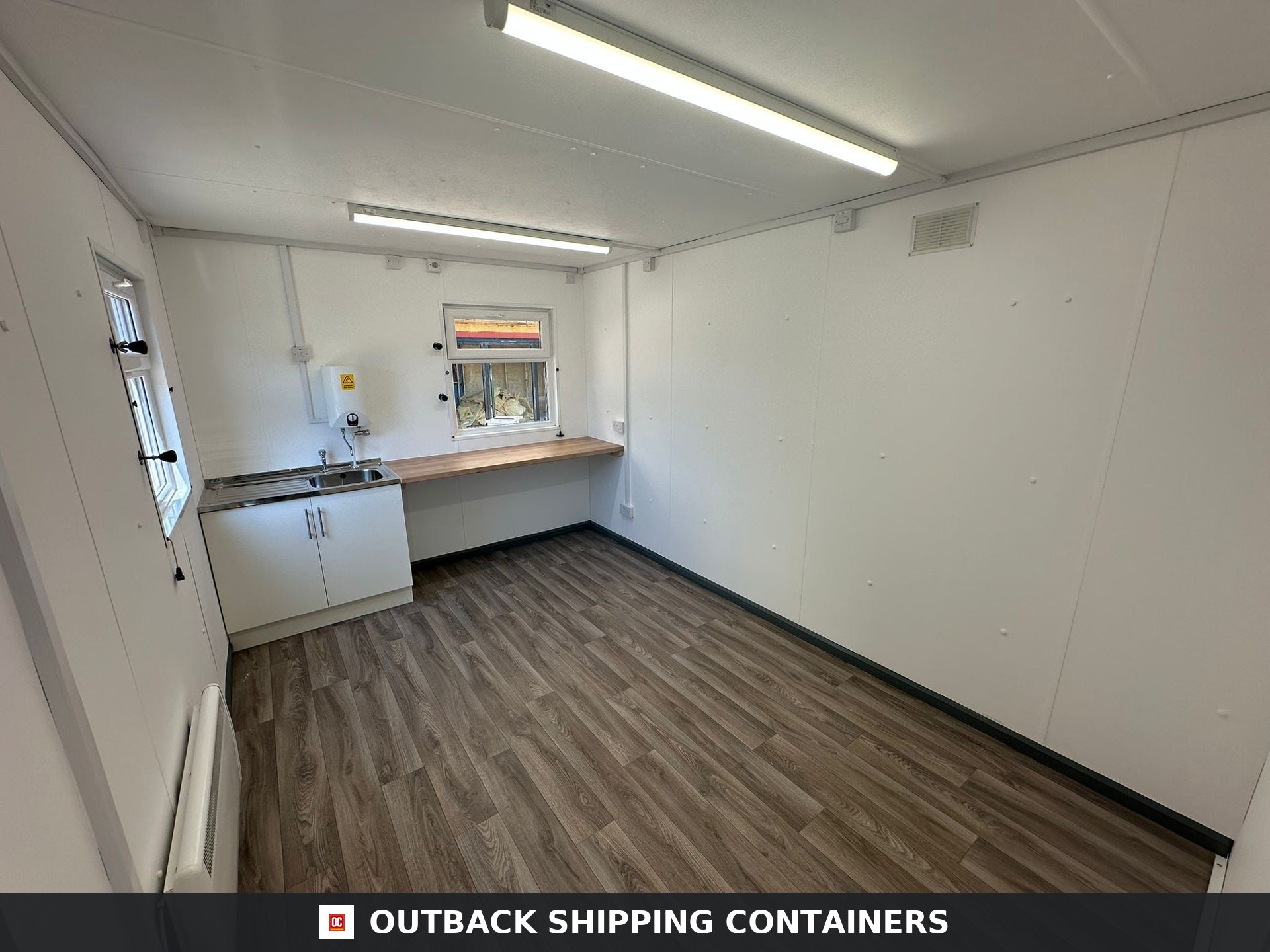 32 x 10Ft 32x10FT for Sale — Three-Quarter Angle View | Outback Shipping Containers Refurbished office cabin interior with wood-style flooring, white walls, kitchen sink, and overhead LED lighting