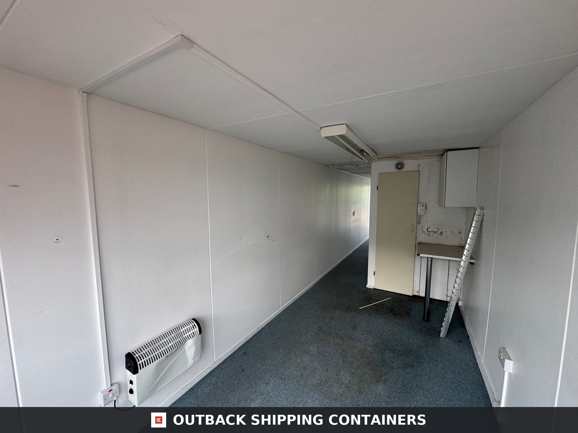 Converted Shipping Container 40 Ft 40FT — Interior Detail | Outback Shipping Containers Interior view of a 40ft container office featuring white walls, blue carpet, and a wall-mounted electric heater