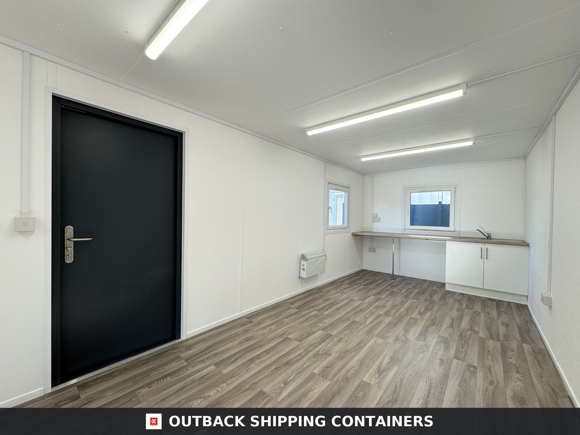 32x10ft Cabin for Sale — Three-Quarter Angle View | Outback Shipping Containers Refurbished 32x10ft cabin interior with wood flooring black door and white kitchenette