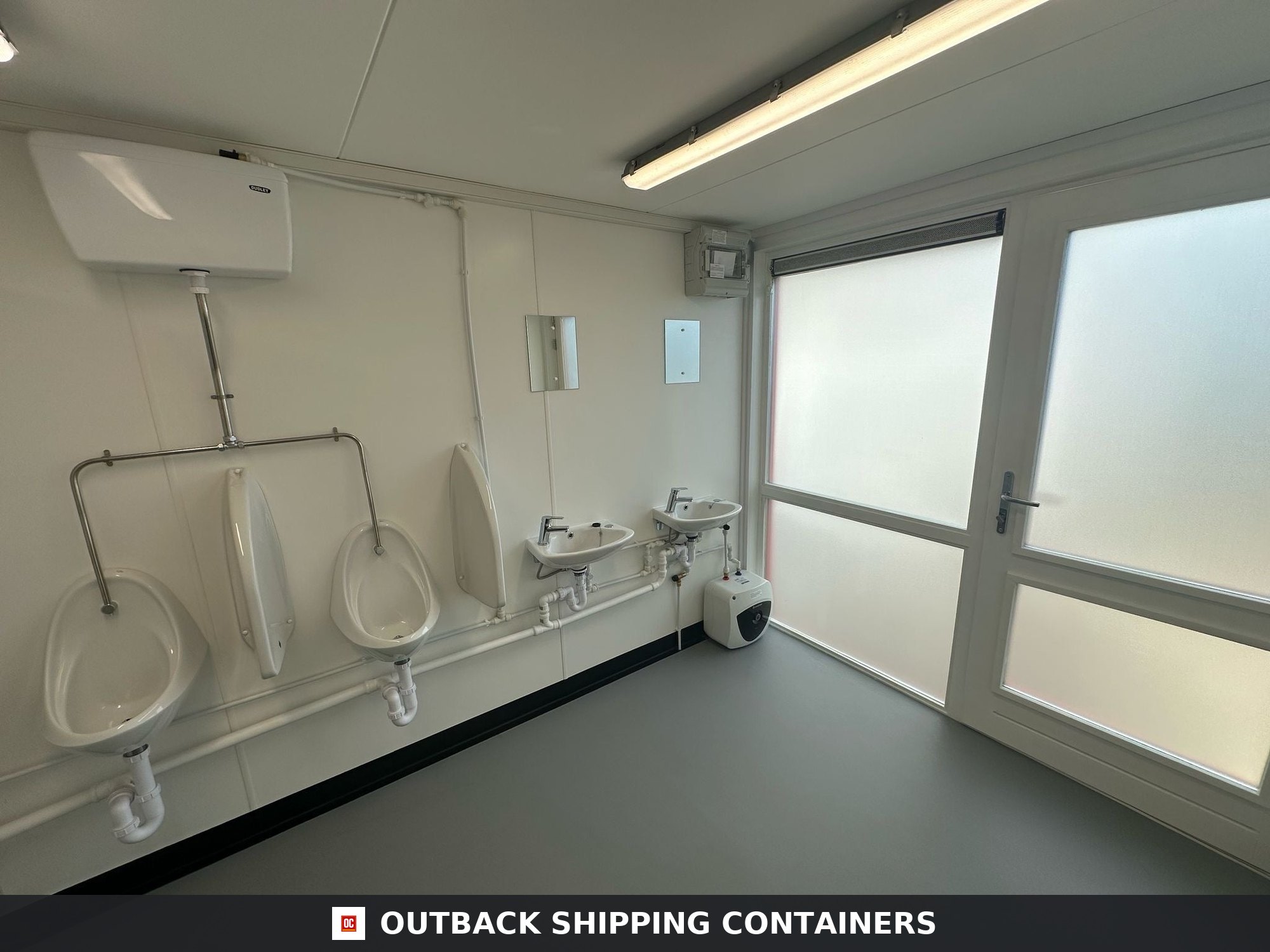 40x8ft for Sale — Corner Casting and Frame Detail | Outback Shipping Containers 2 Interior of a refurbished 40ft shipping container restroom with two urinals, two sinks, and frosted glass doors