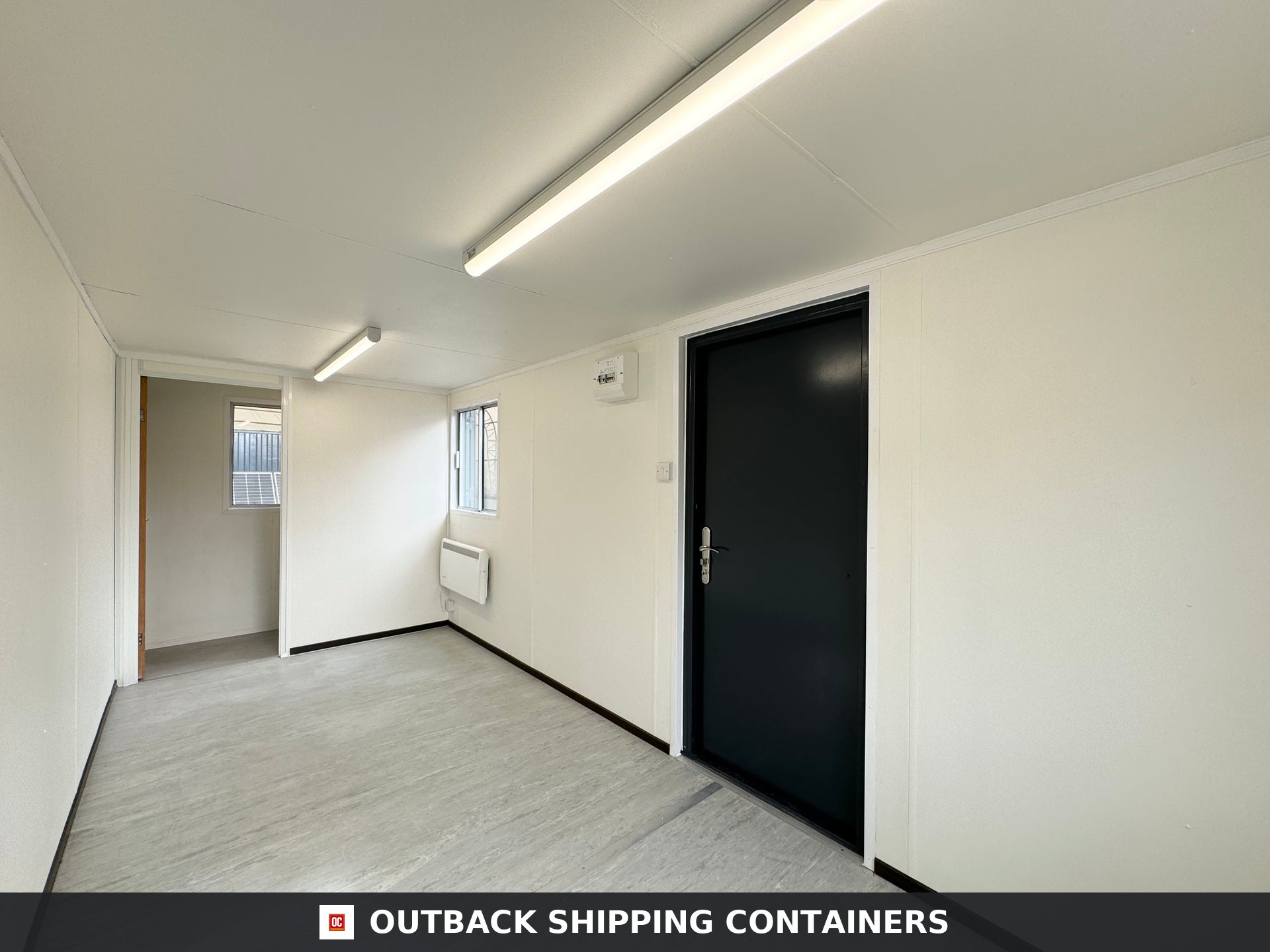 21x8ft for Sale — Three-Quarter Angle View | Outback Shipping Containers 2 Interior view of a refurbished 21x8ft portable office cabin showing white walls, black steel door and fluorescent lights