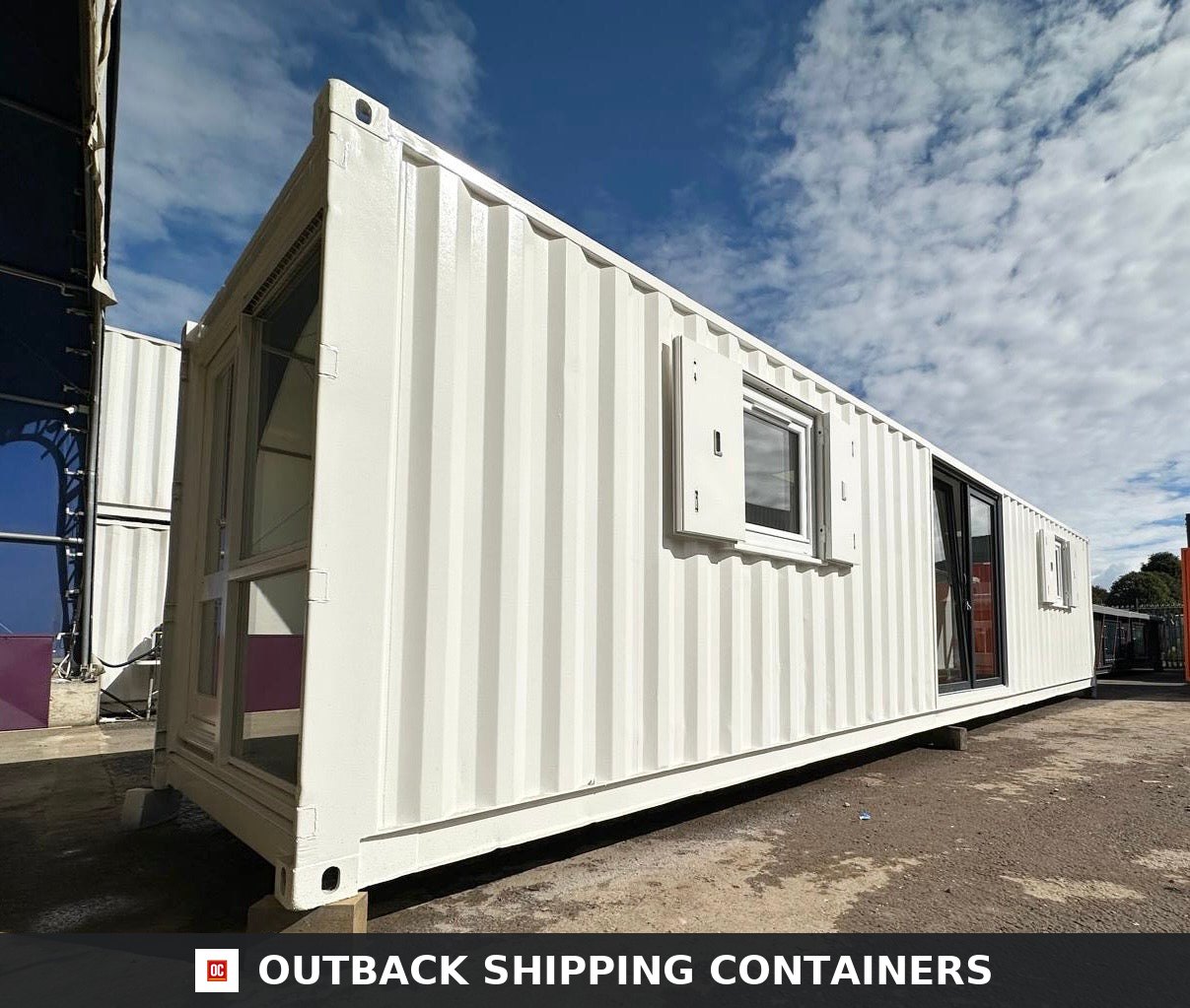 White 40ft converted shipping container office with glass sliding doors and windows under a bright blue sky