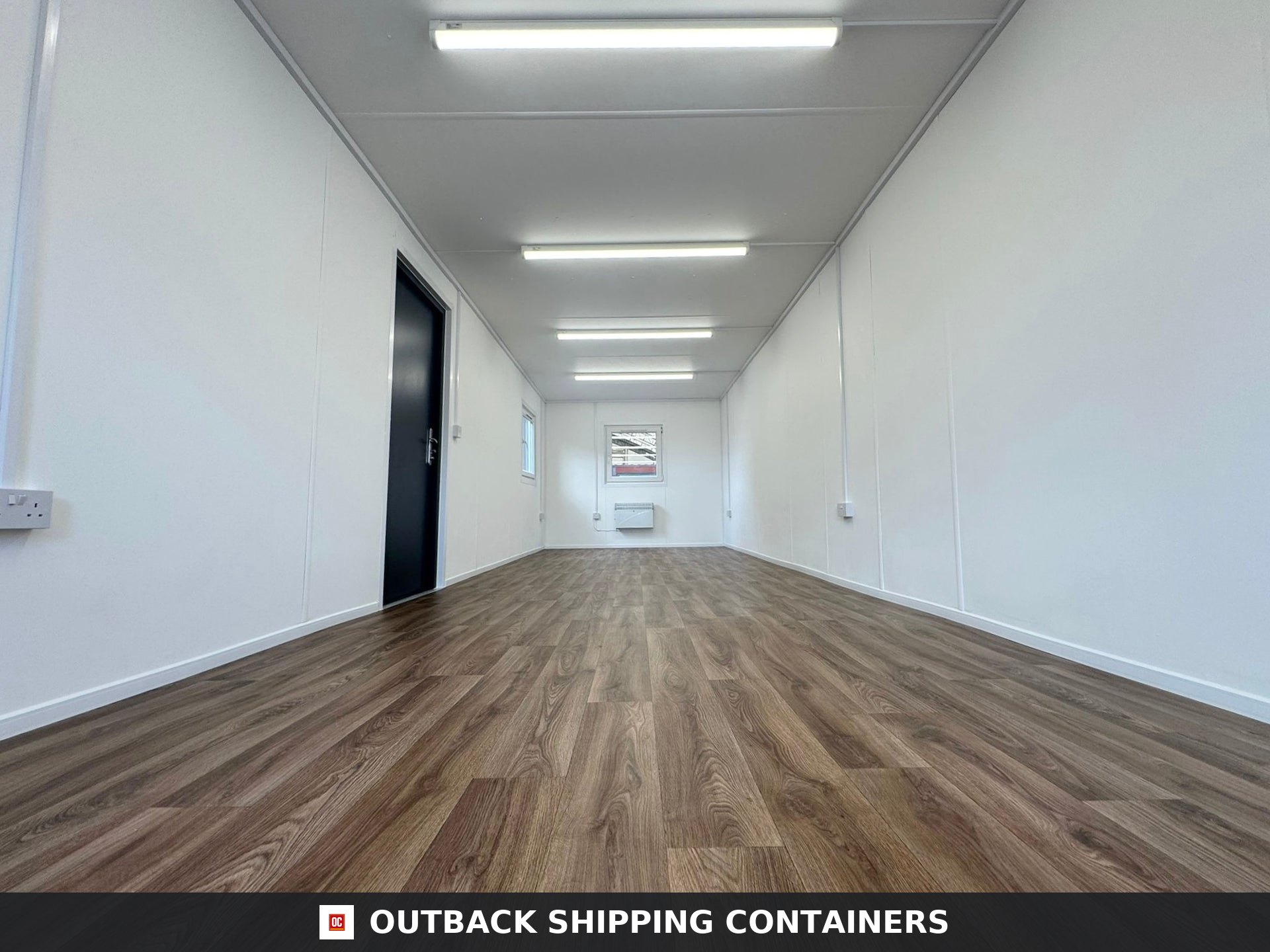 32ft Cabin for Sale — Rear Exterior View | Outback Shipping Containers Interior of 32ft open plan office cabin showing wood effect flooring white walls fluorescent lights and a black door