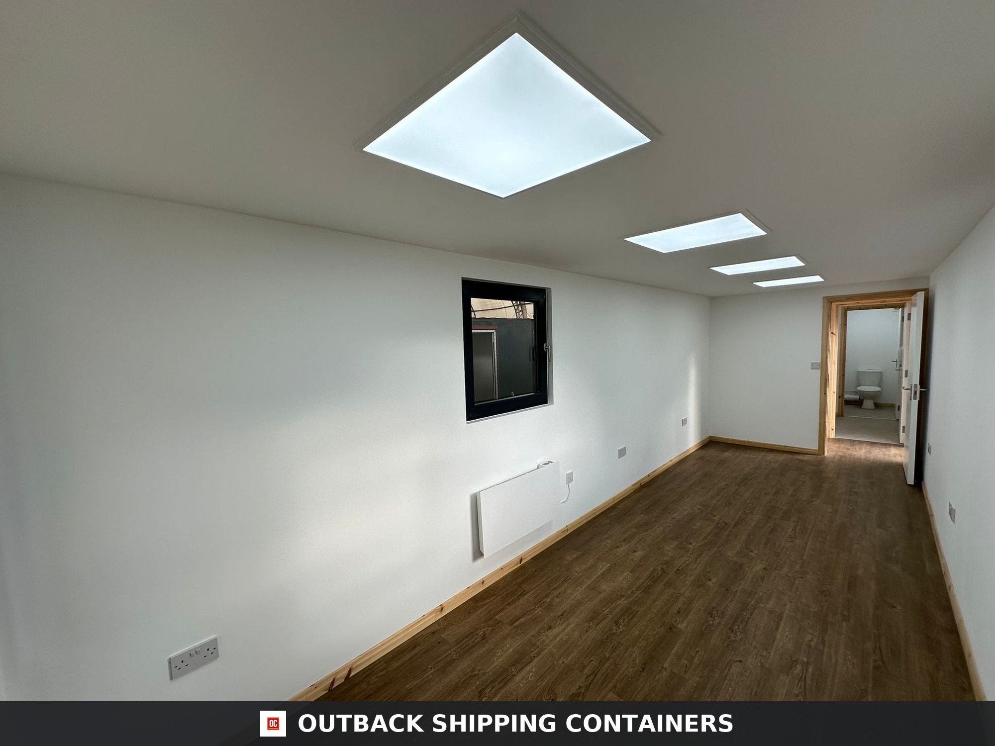 Interior of a 40ft shipping container office with white walls, wood floors, and square LED ceiling lights
