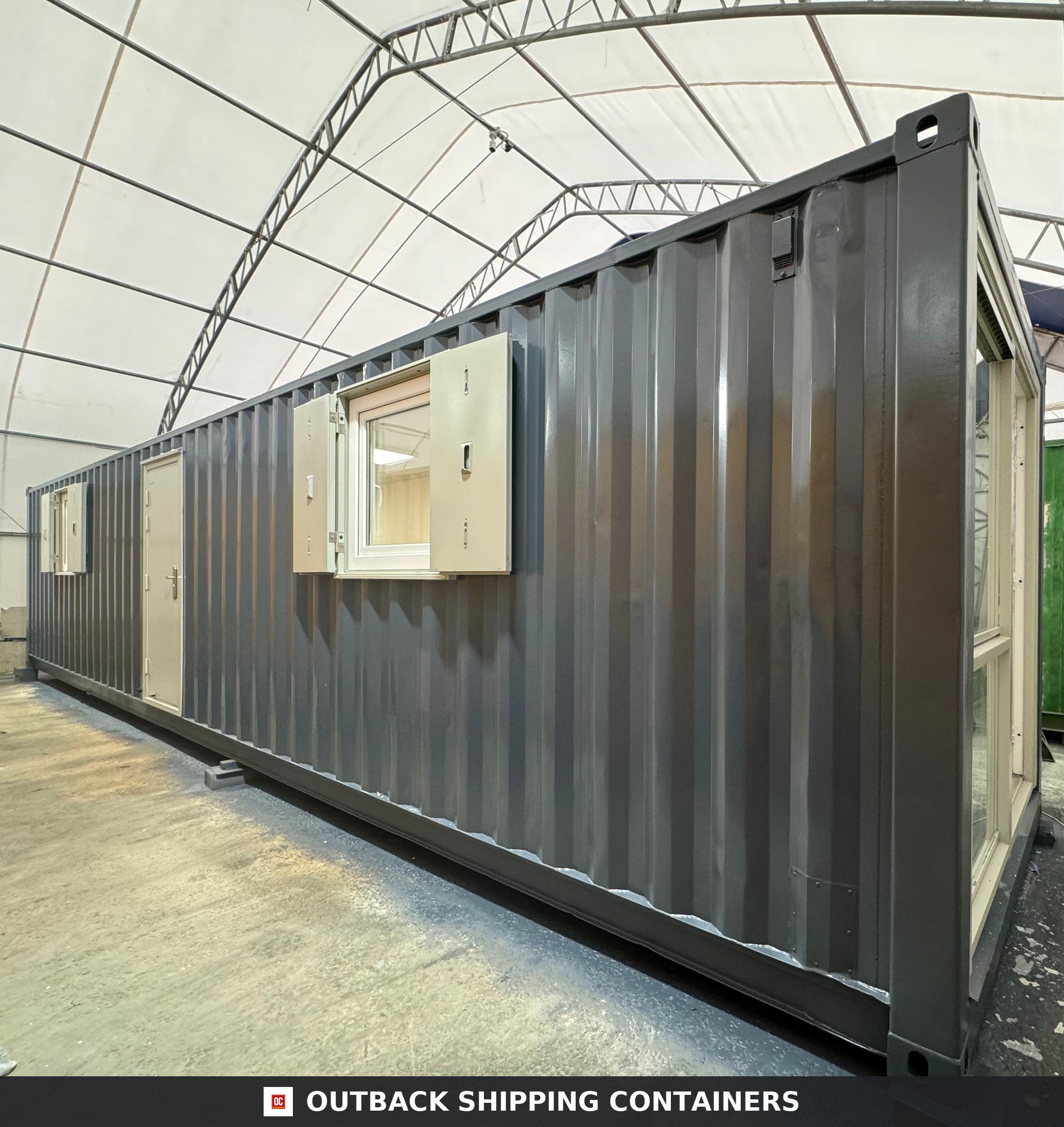 Dark grey 40ft converted shipping container office with beige windows and side entry door inside a warehouse
